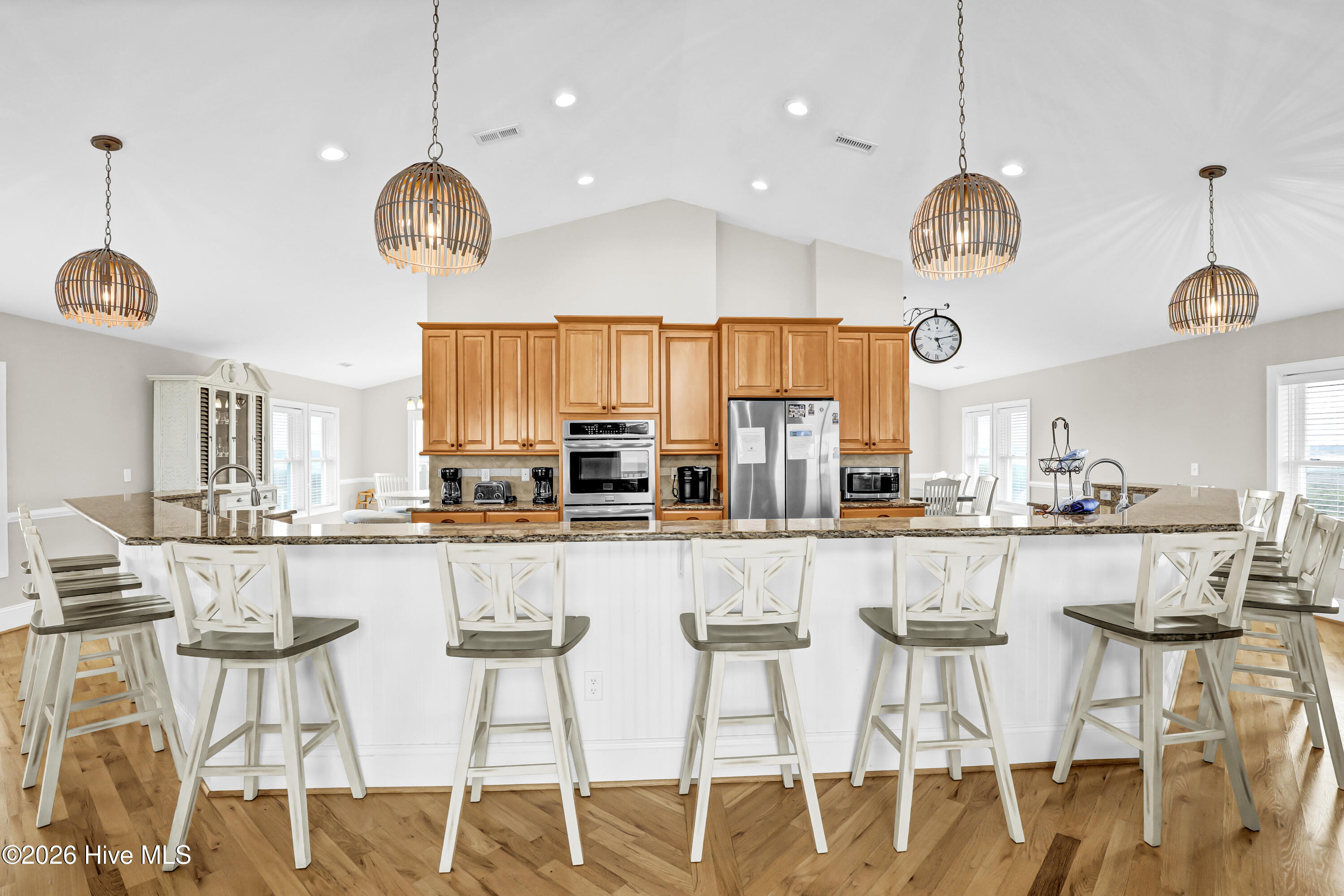 Kitchen with a large island, white bar stools, warm wood cabinetry, and stainless steel appliances.
