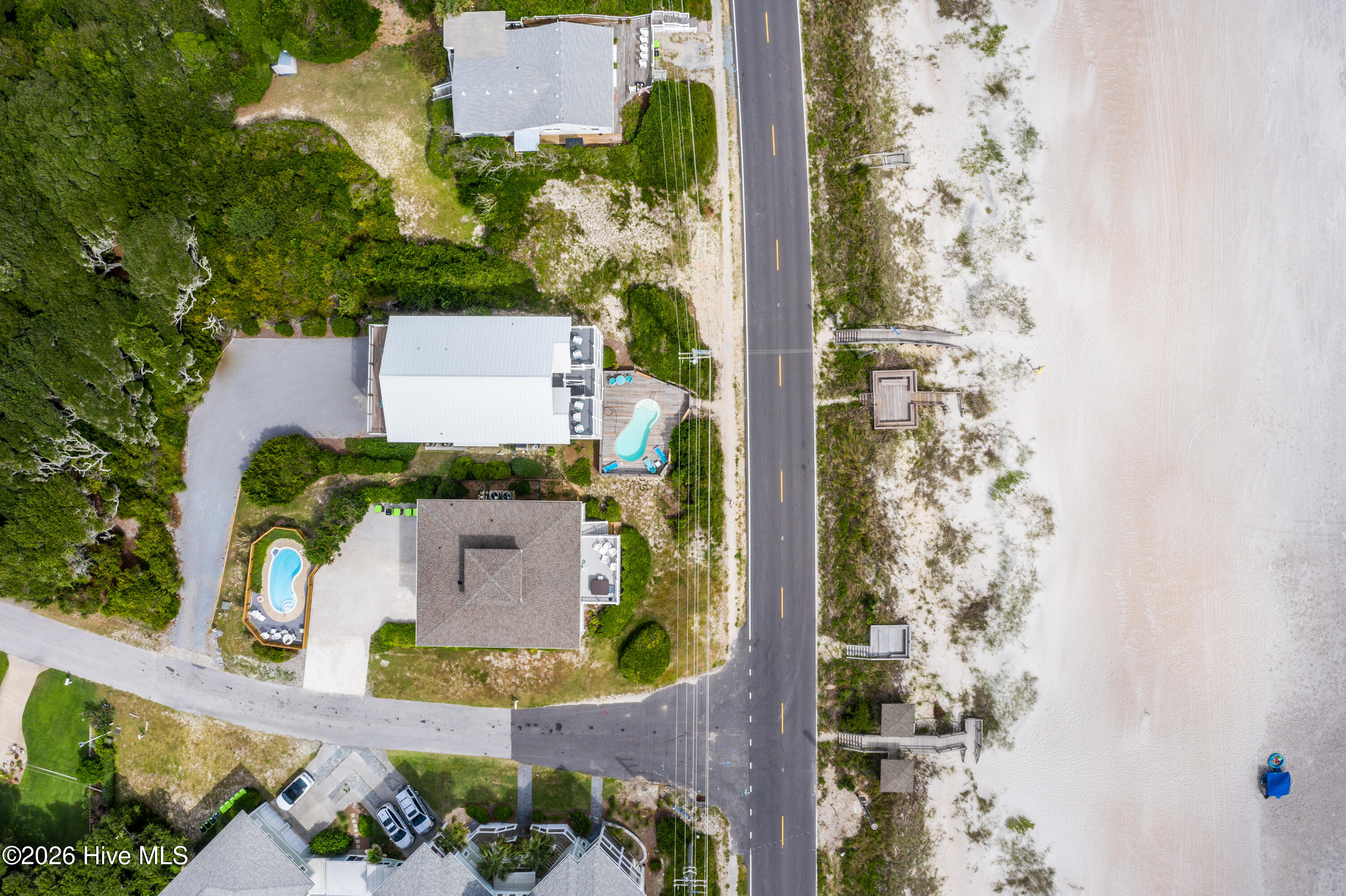 Aerial view of a coastal home with a private pool beside a road and sandy beach.