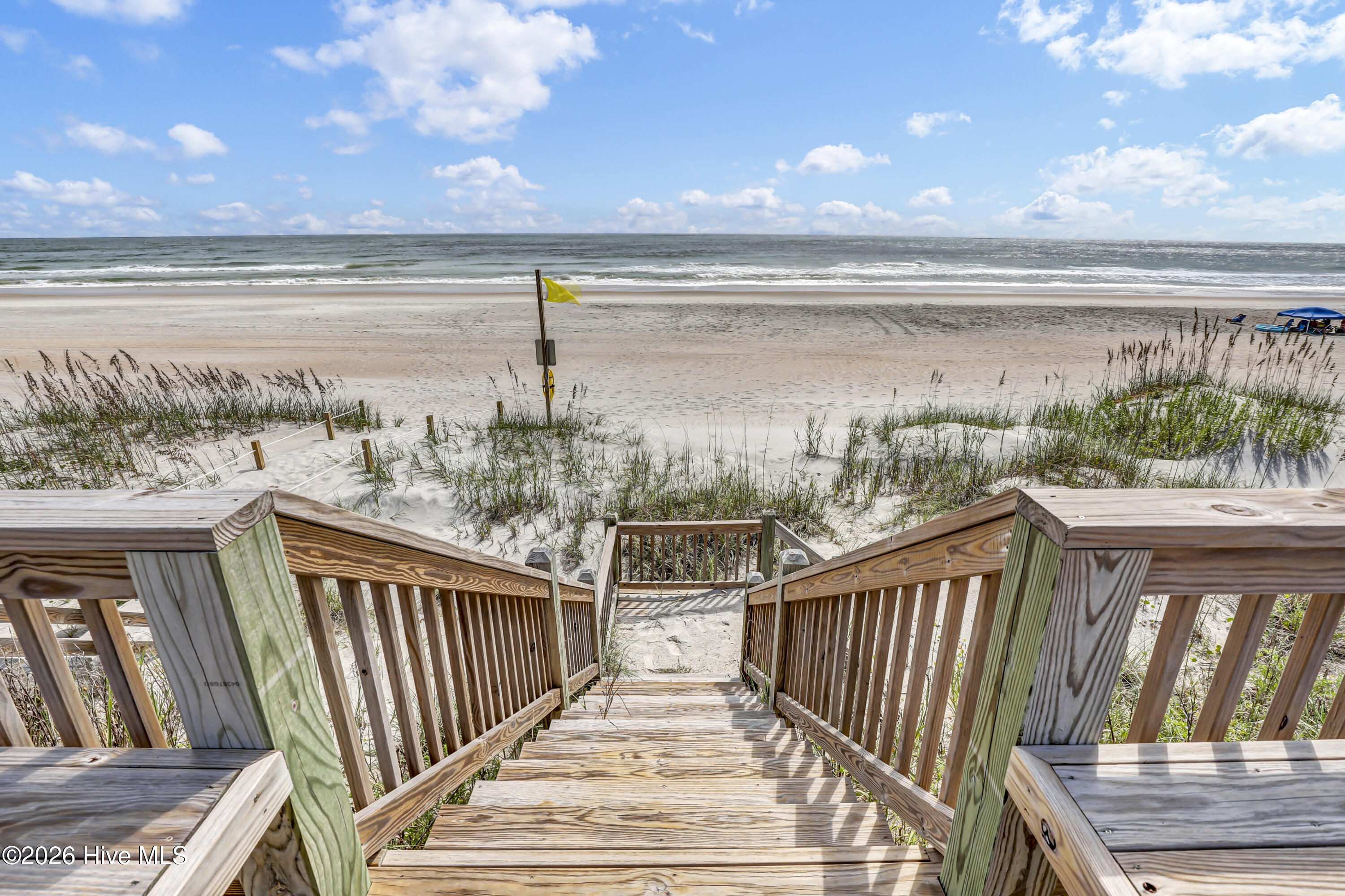 Wooden beach stairs descend through dunes to a sandy shore and ocean.