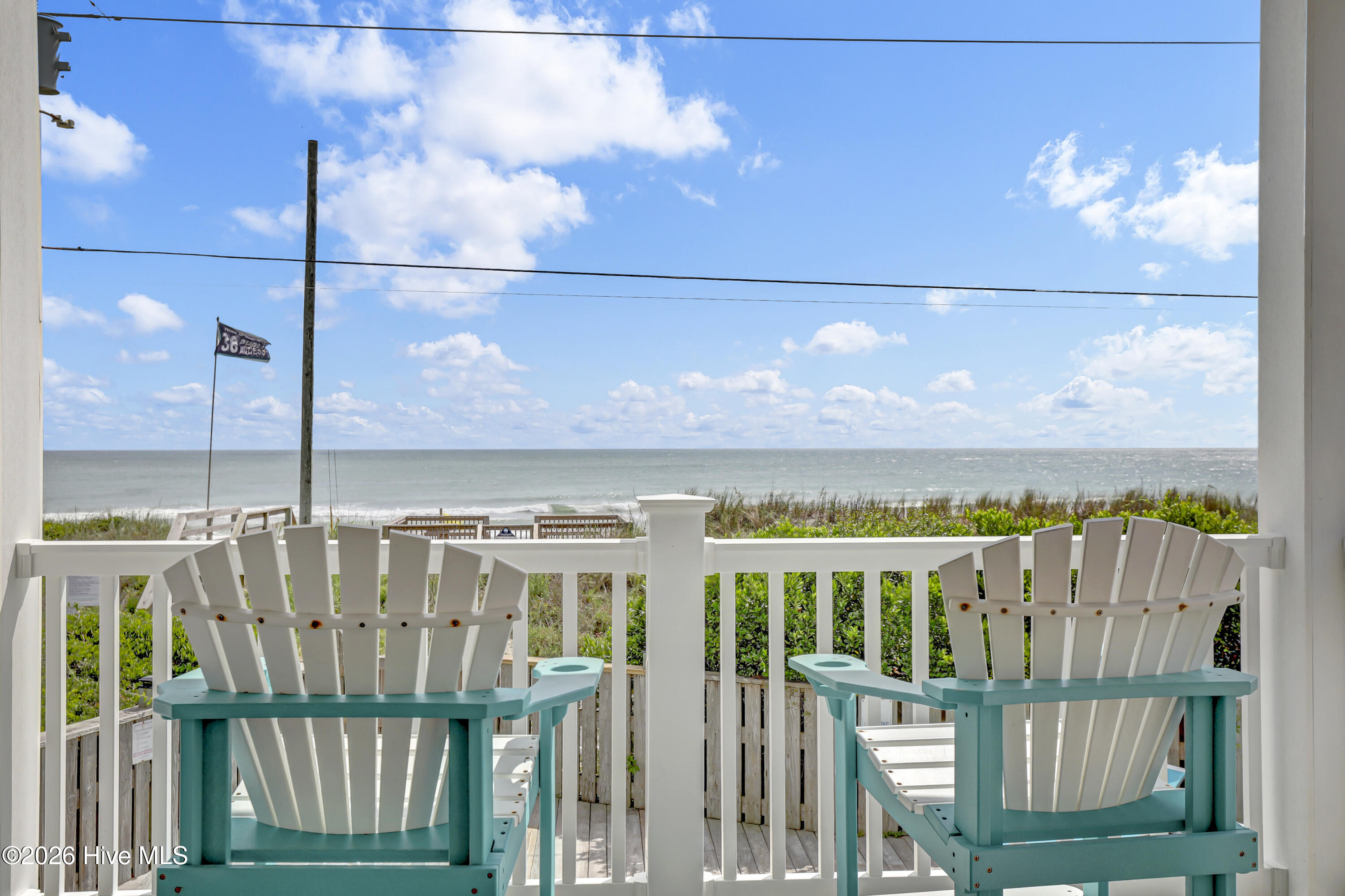 Seaside deck with two white Adirondack chairs overlooking the ocean and dune grass.
