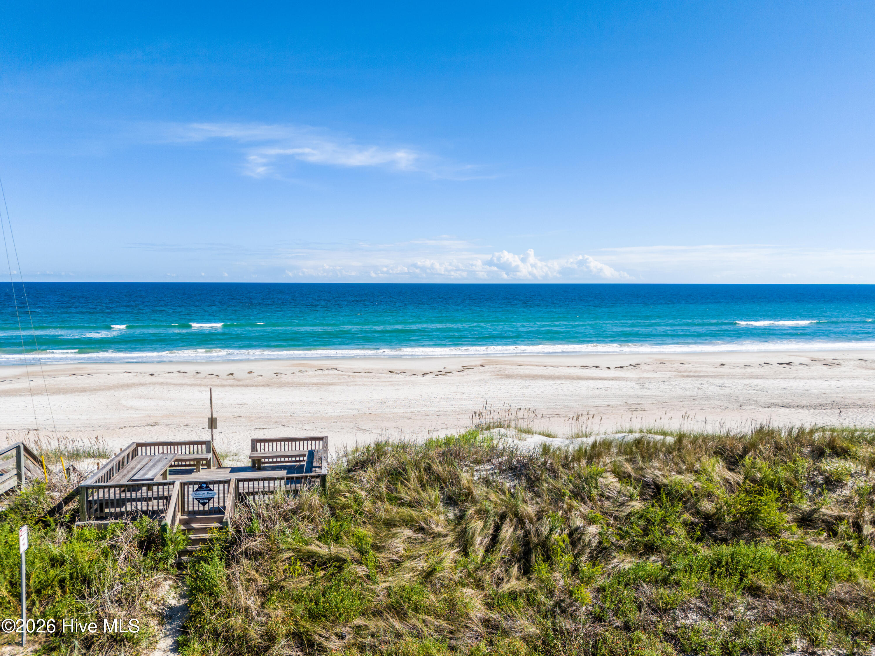 Beach and ocean with turquoise waves, dune grass, and a wooden beach-access stairway.