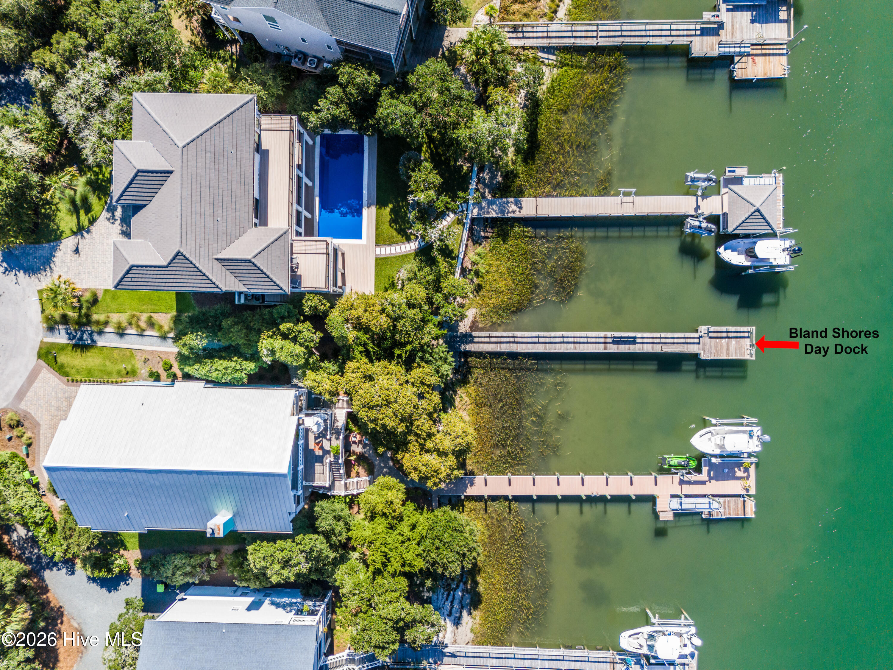 Aerial view of waterfront homes, private docks, boats, and a pool beside a green waterway.