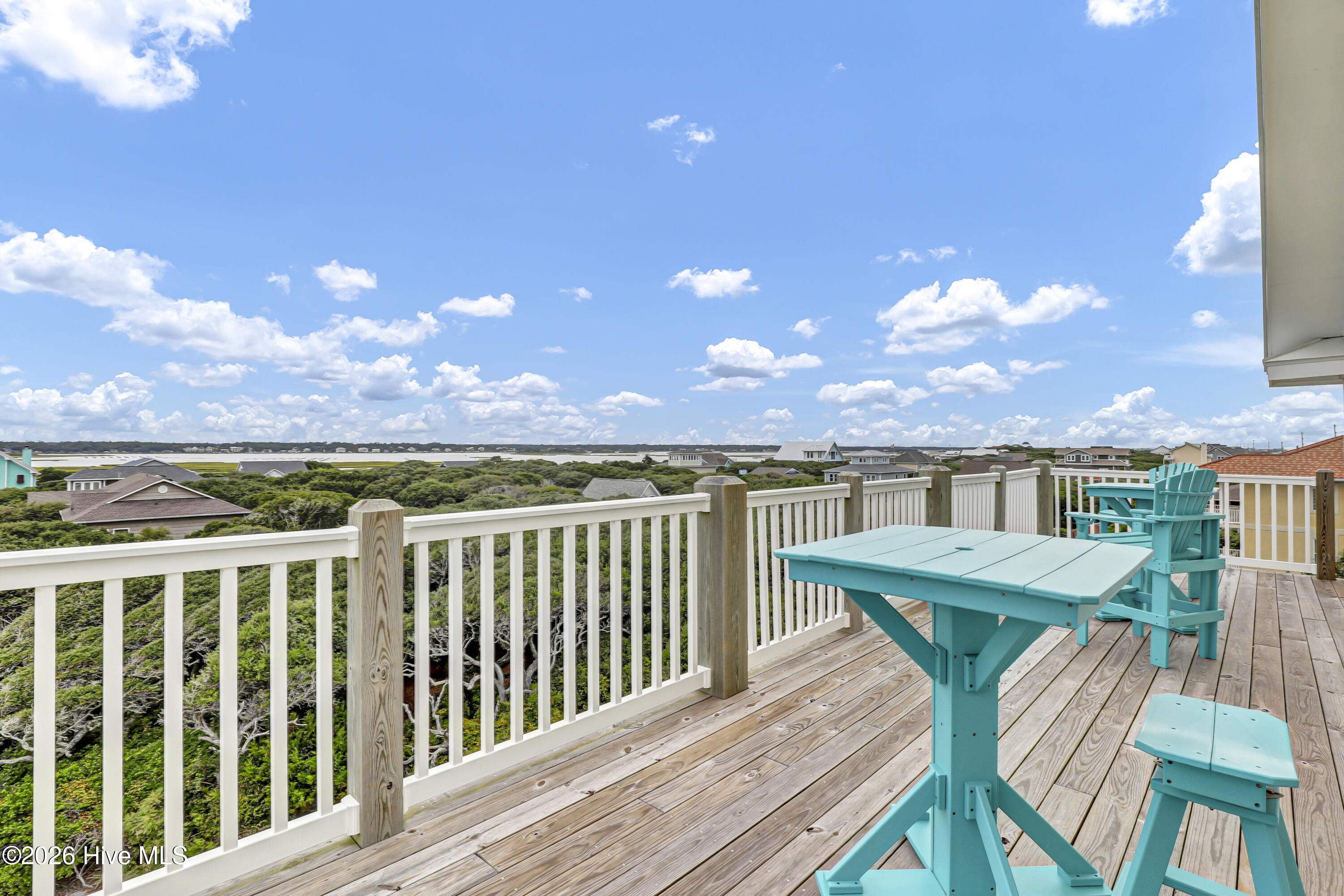 Wood deck with turquoise outdoor furniture overlooking coastal marsh, water, and neighboring homes.