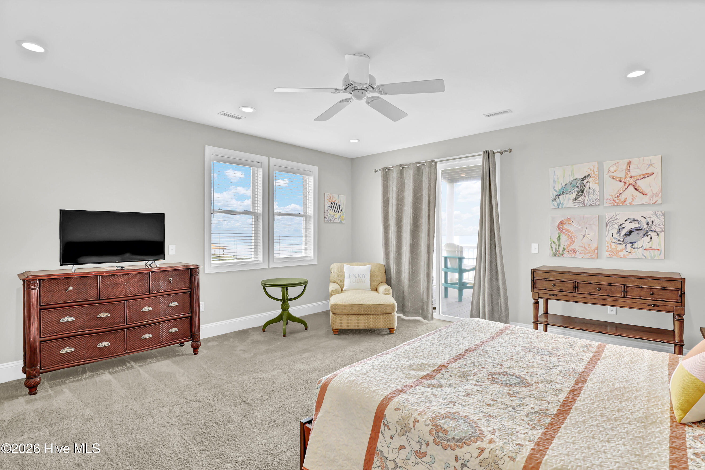 Coastal bedroom with a patterned quilt, ocean-view windows, and a glass door to the balcony.