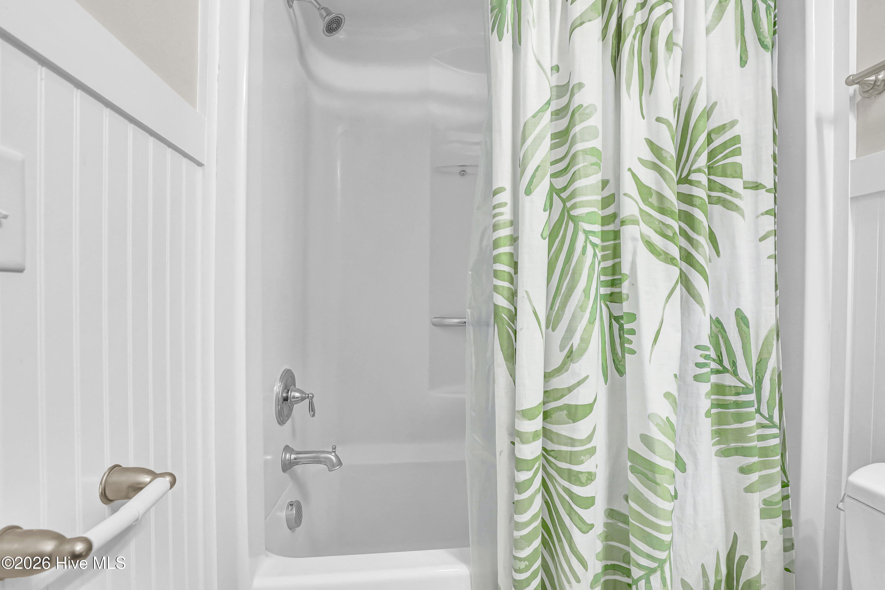 Bathroom tub and shower with chrome fixtures and a green leaf-patterned curtain.
