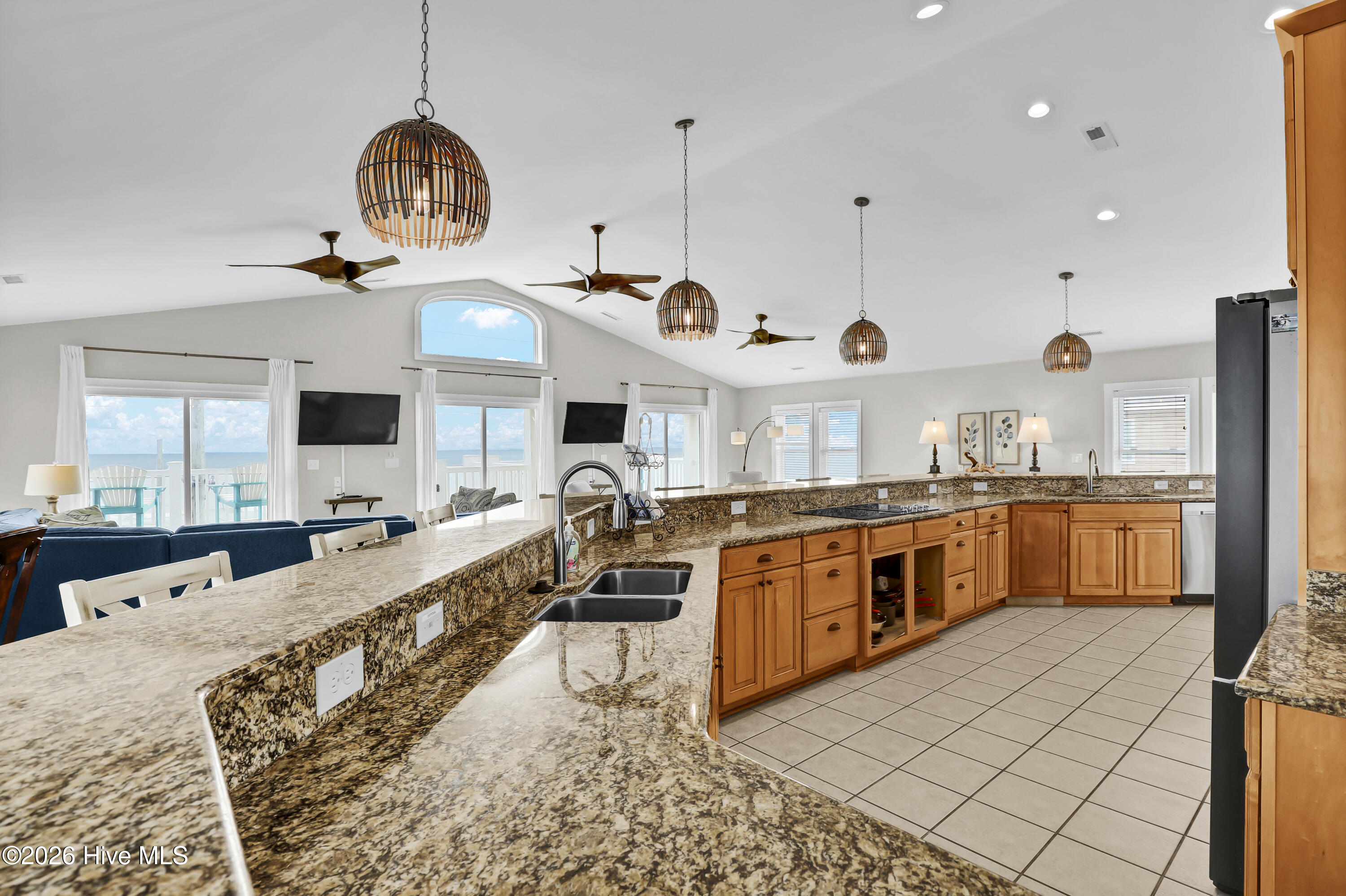 Kitchen with granite counters and warm wood cabinets, opening to a living area with ocean views.