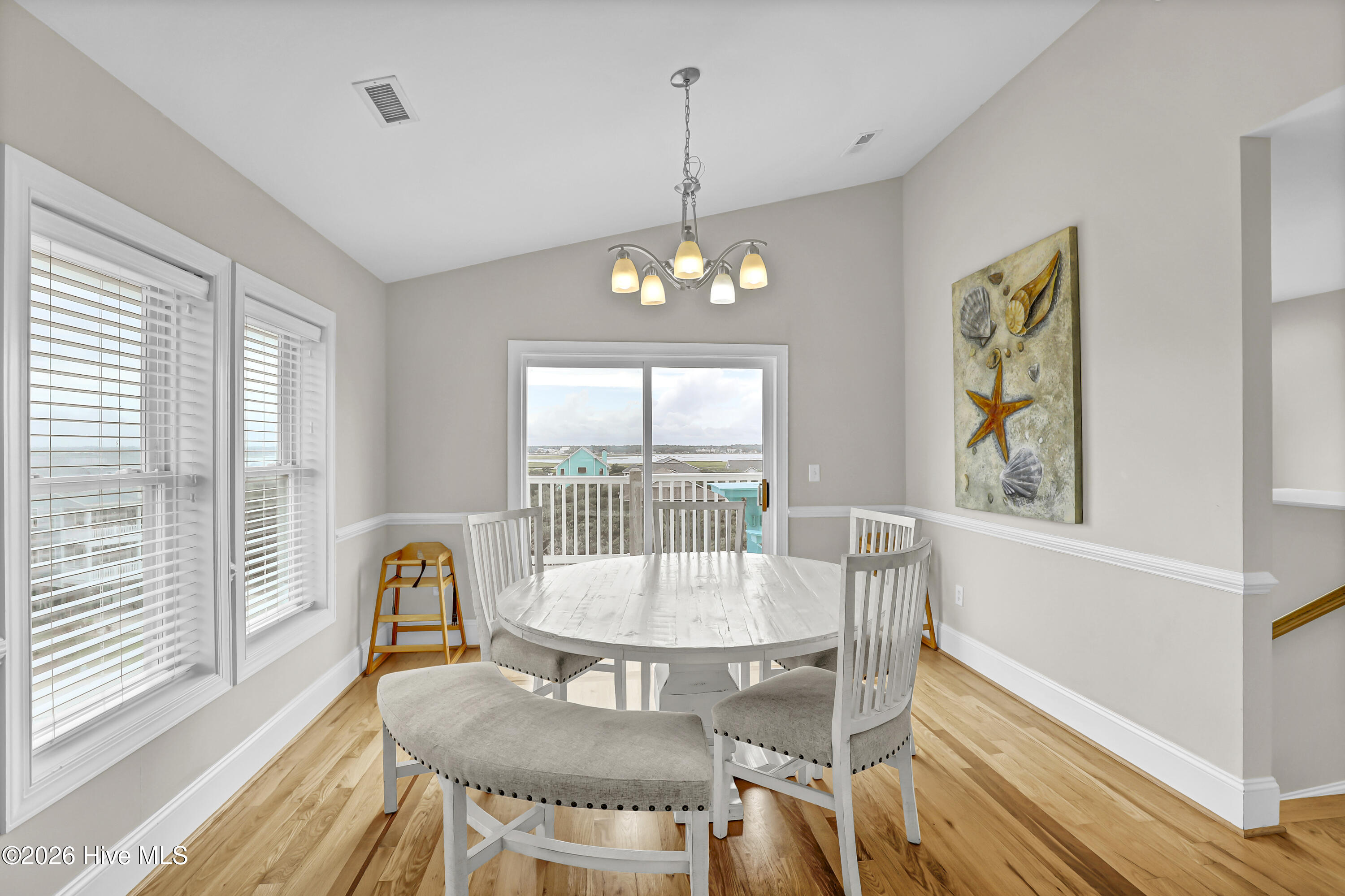 Dining room with a white oval table, coastal wall art, and water views through the windows.