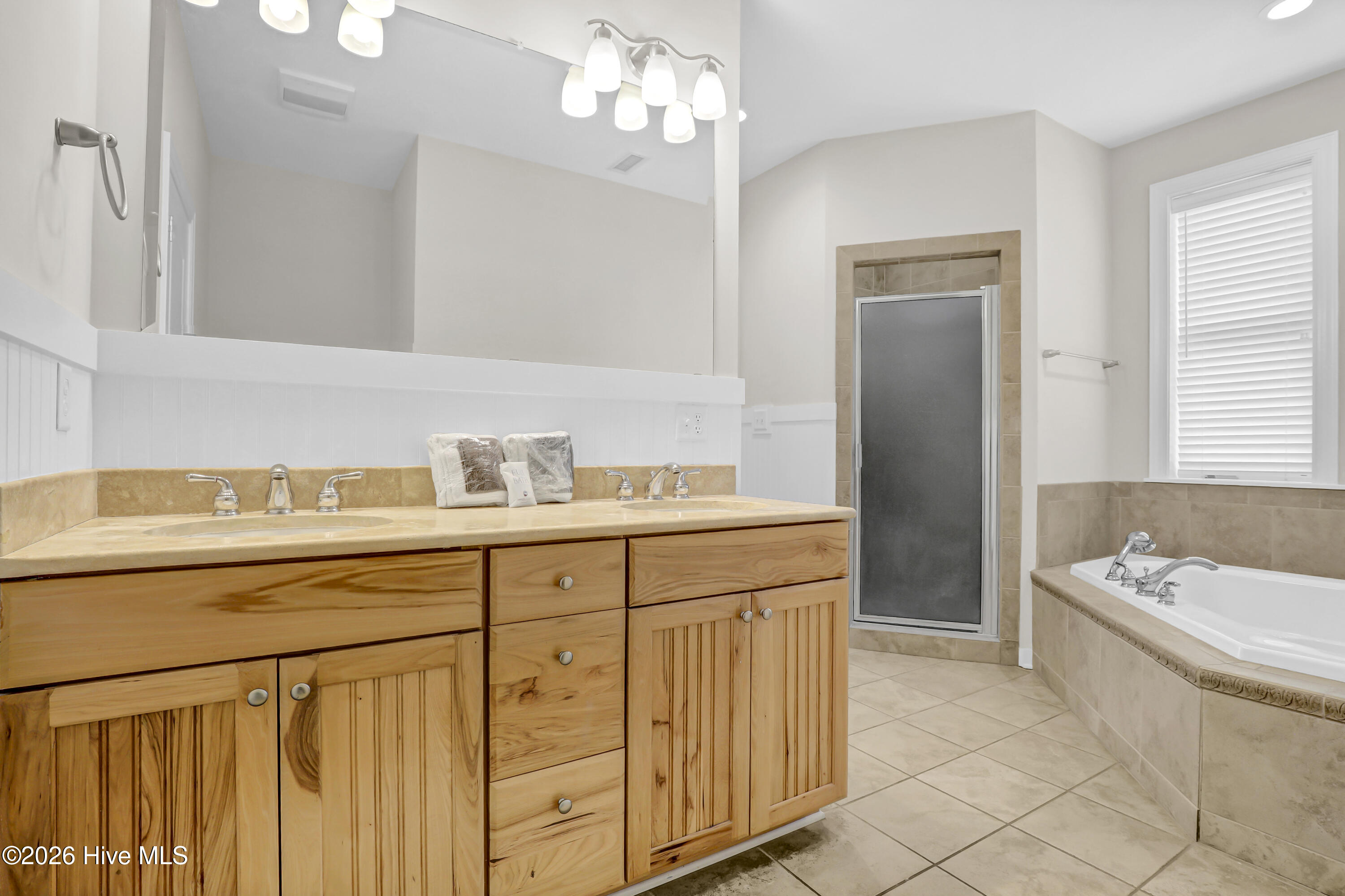 Bathroom with a long wood vanity, glass shower, and built-in soaking tub beside a window.