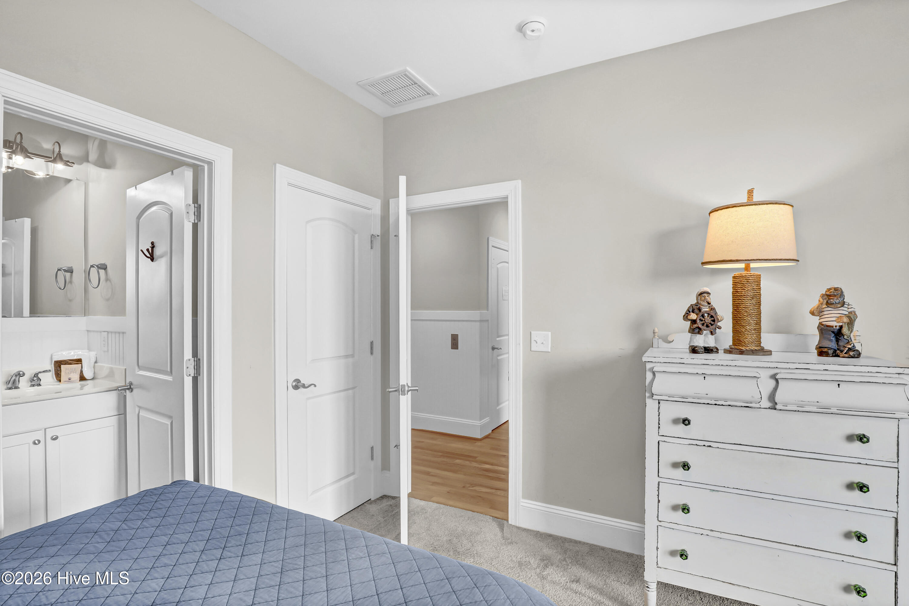 Bedroom with blue quilted bed, white dresser, nautical decor, and an open doorway to the bathroom.