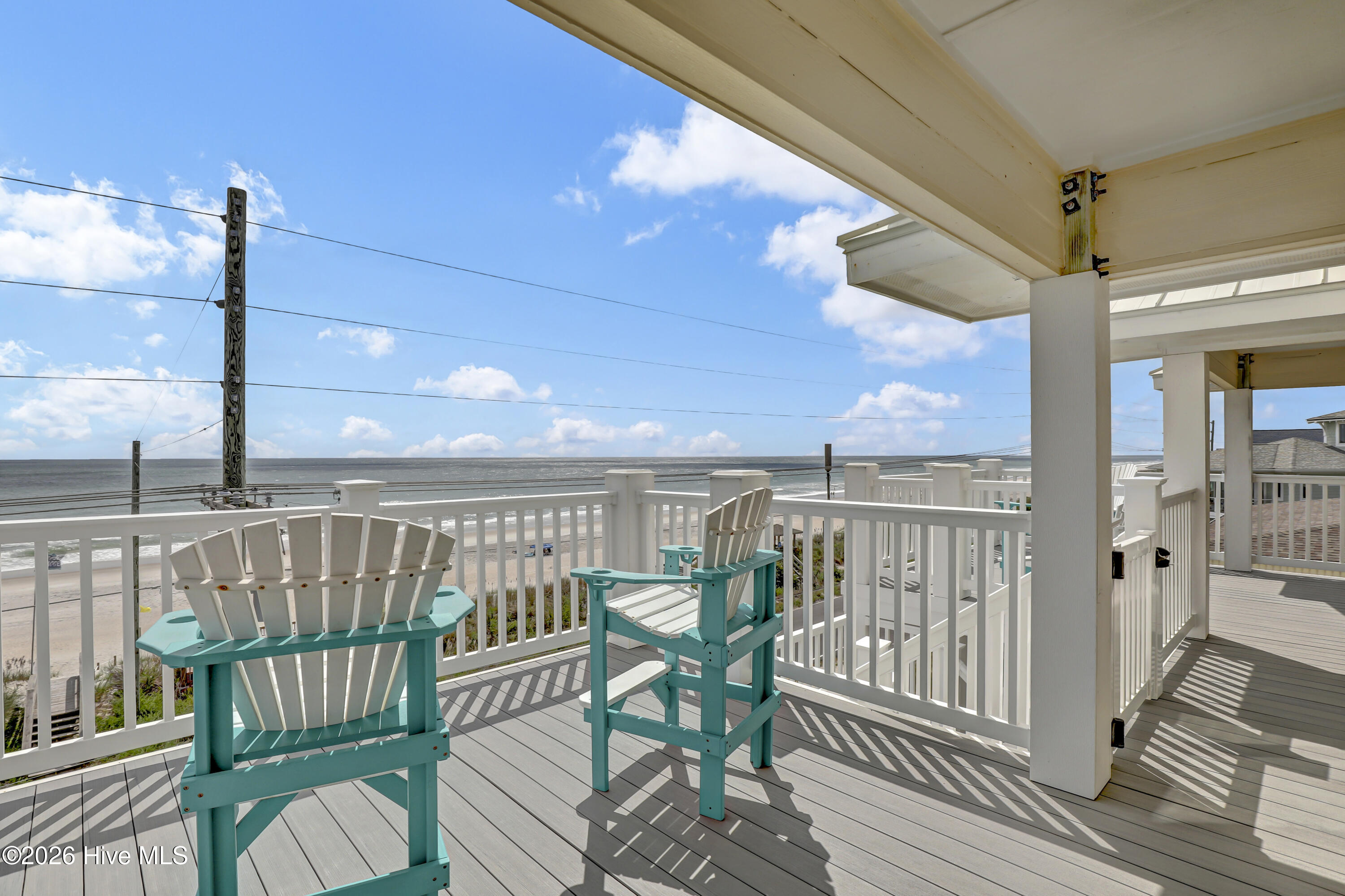 Covered oceanfront deck with turquoise Adirondack chairs overlooking the beach and water.