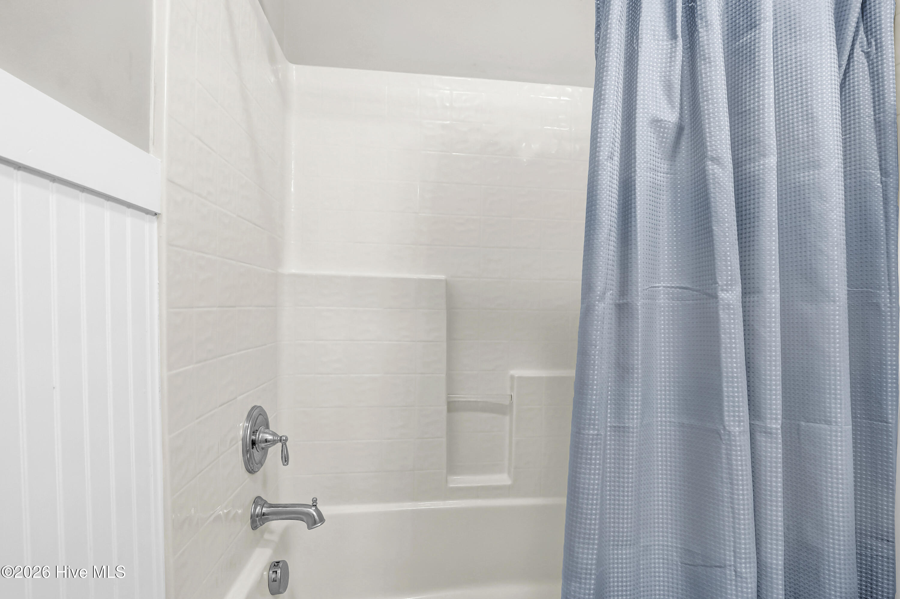 White tiled bathtub and shower with a built-in niche, chrome fixtures, and blue curtain.