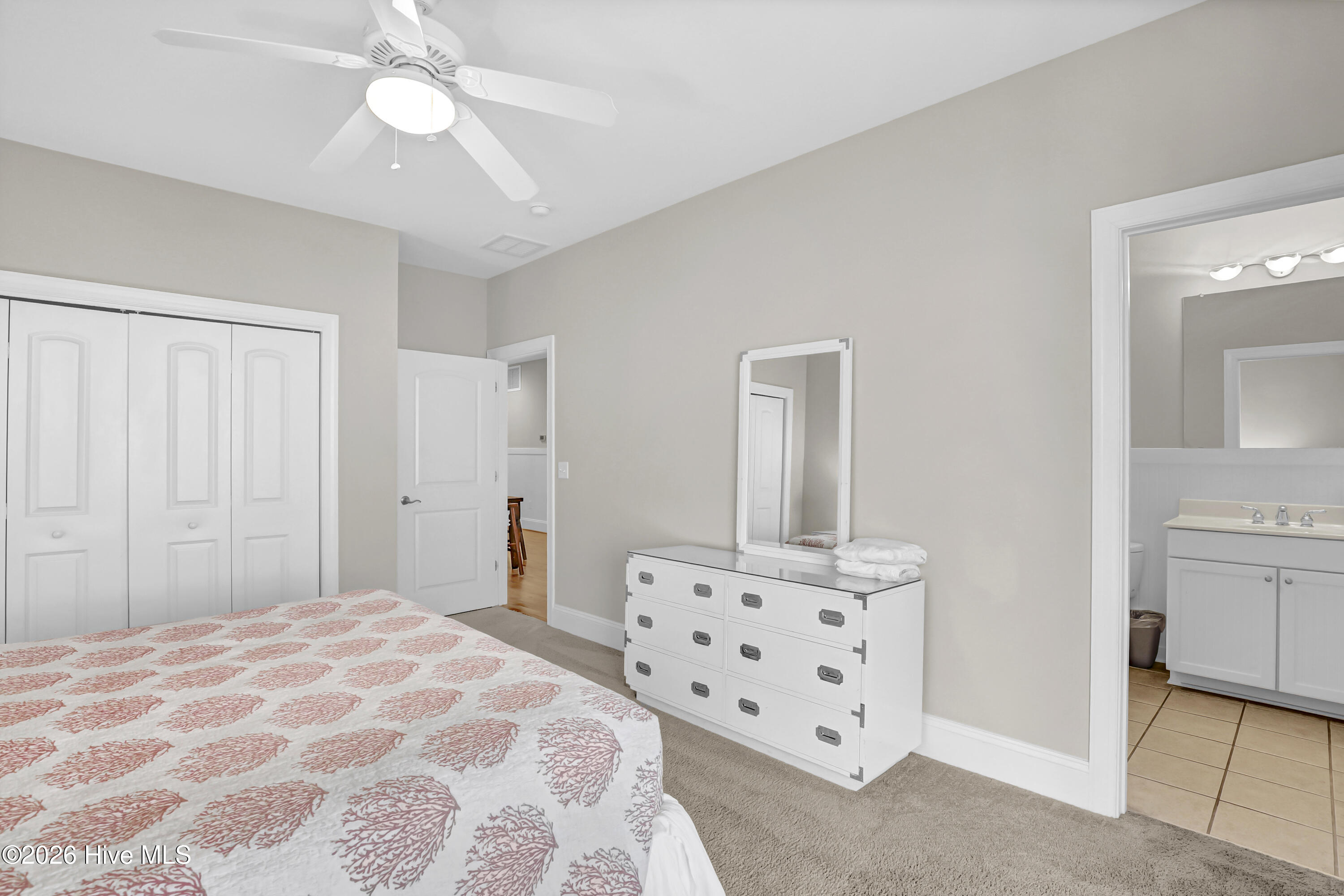 Bedroom with a coral-patterned quilt, white dresser and mirror, and an ensuite bathroom doorway.