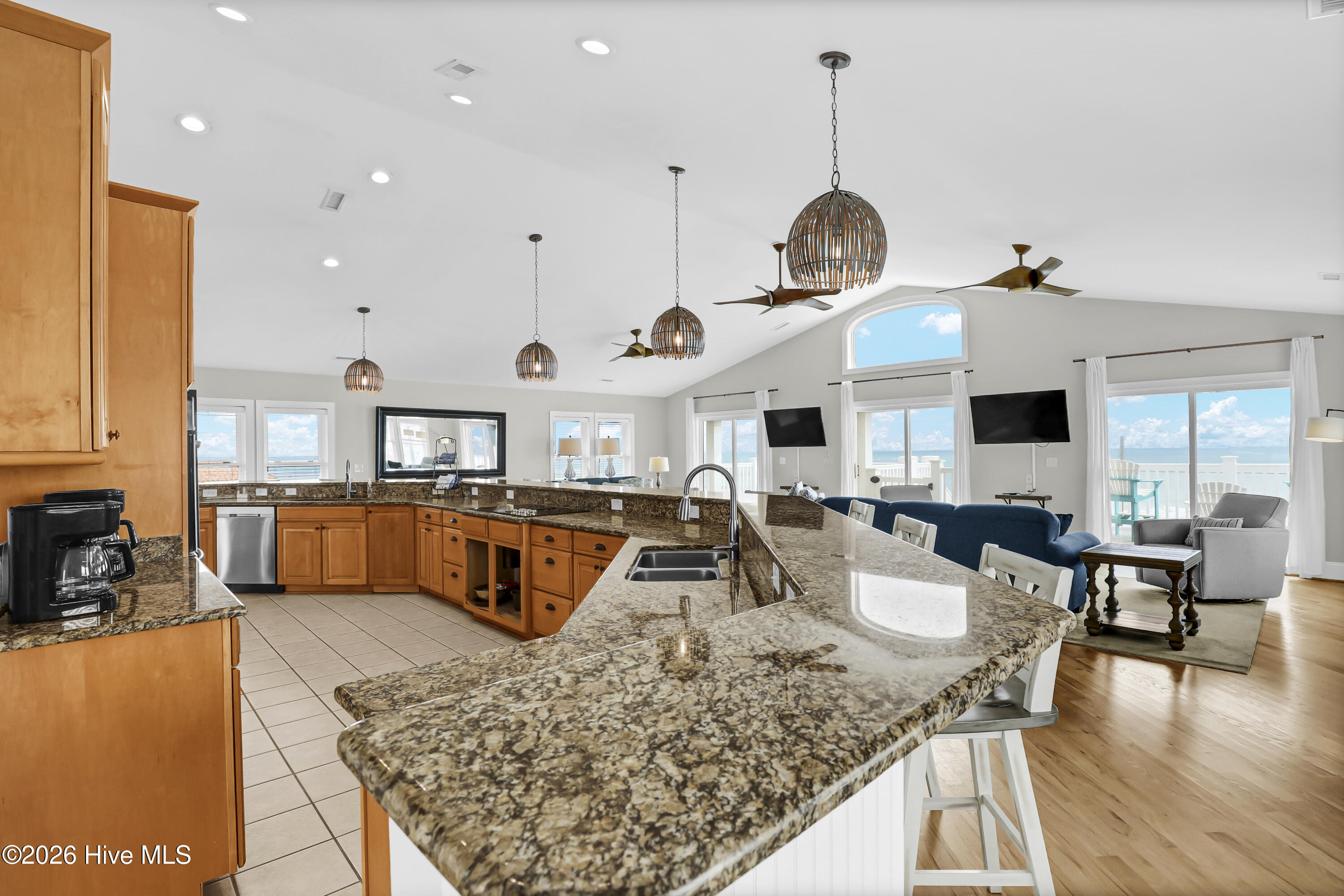 Open kitchen with granite island and wood cabinets, adjoining a living area with ocean views.
