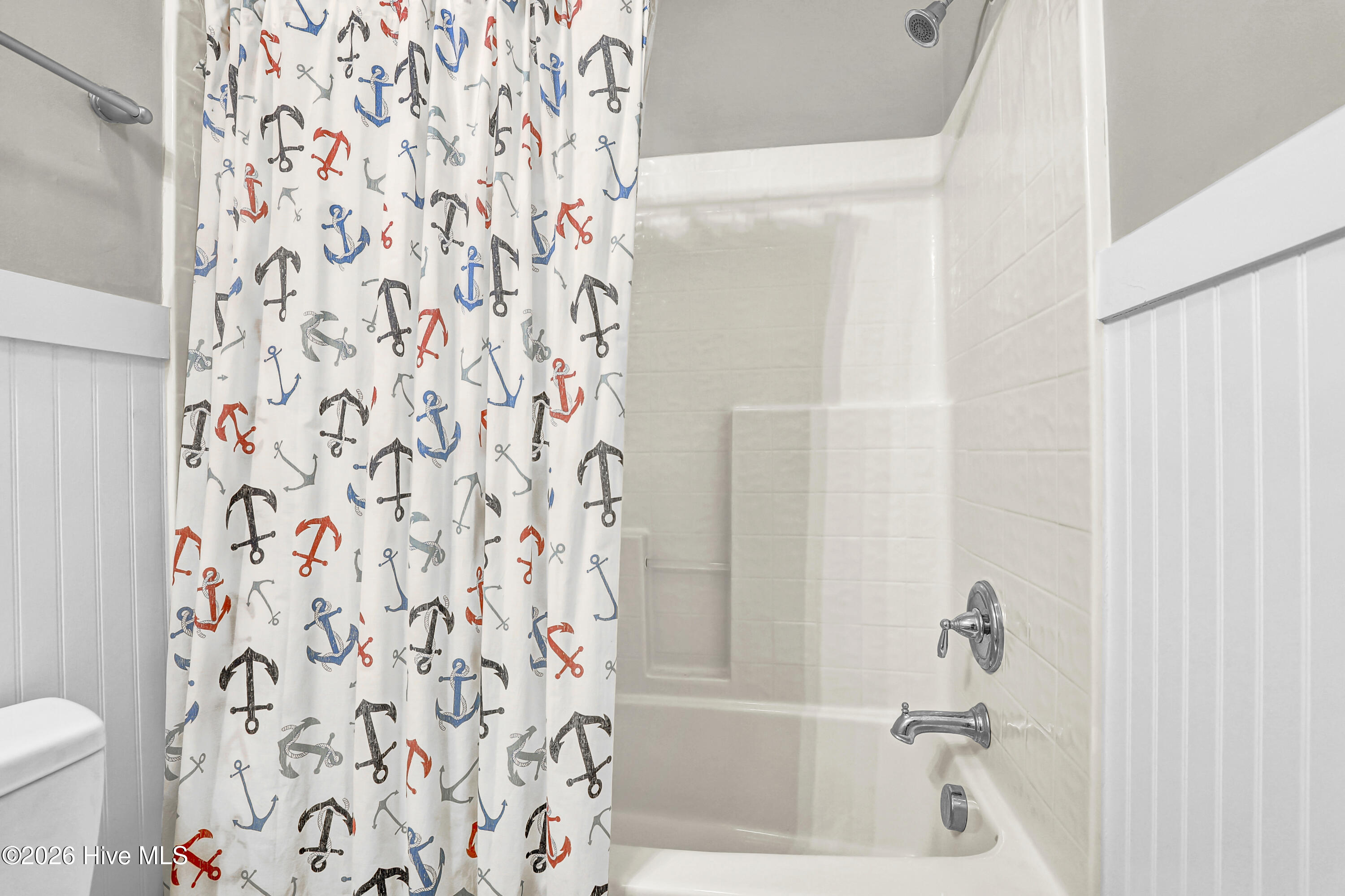Bathroom tub and tiled shower with a colorful anchor-patterned curtain and chrome fixtures.