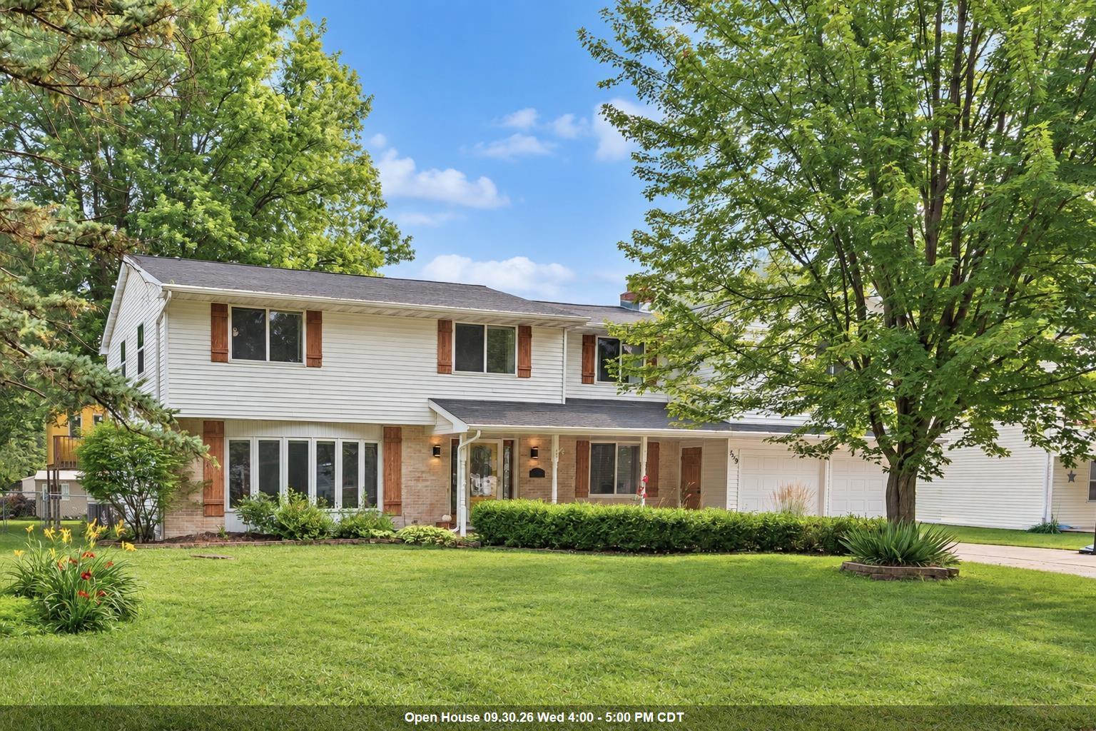 Two-story white-sided home with brick accents, wood shutters, an attached garage, and a leafy front yard.