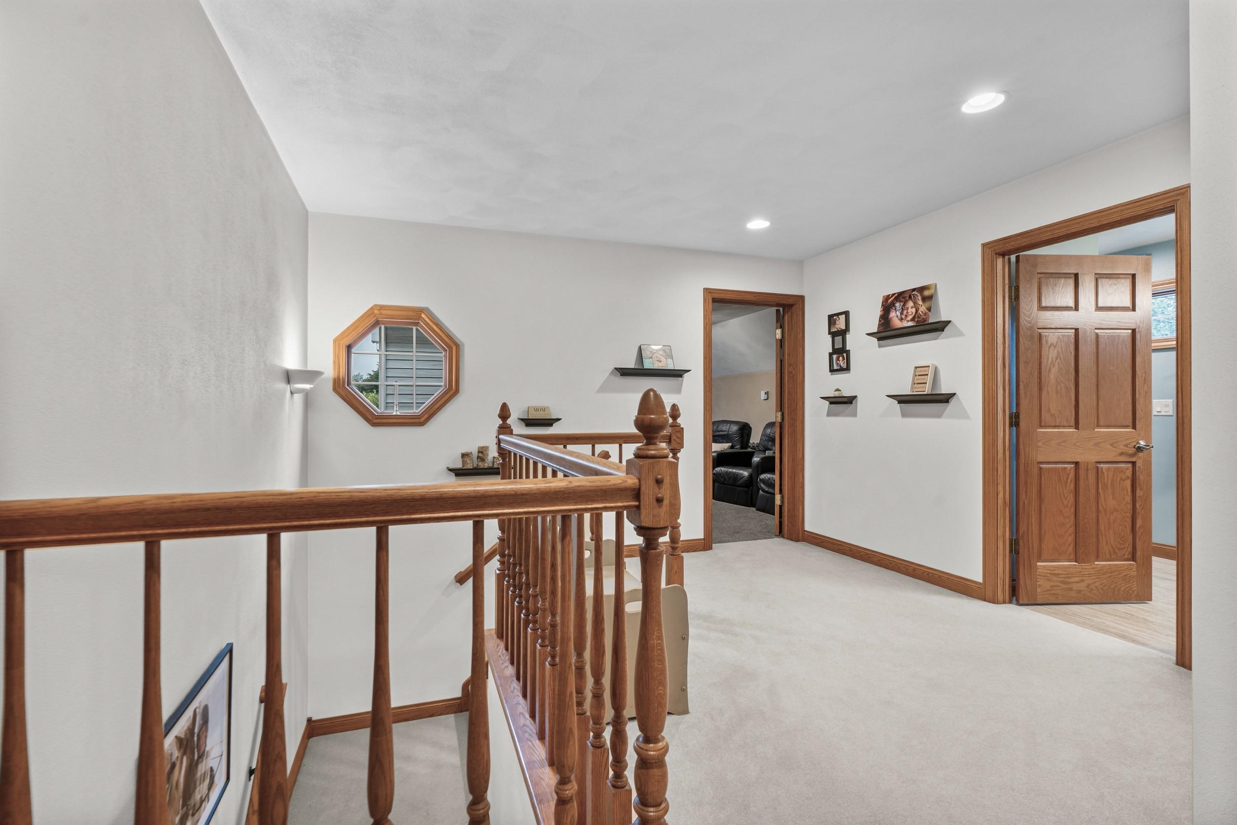 Upstairs landing with a wooden stair railing, octagonal window, and wood-trimmed doorways.