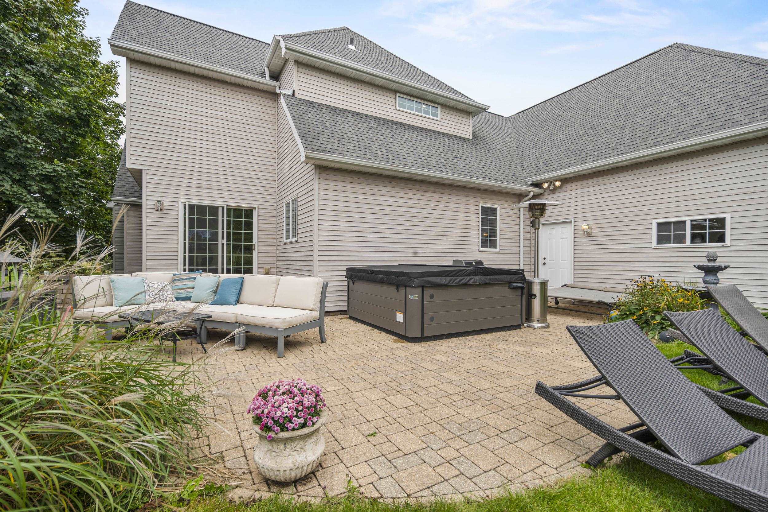 Paved backyard patio with a covered hot tub, sectional seating, and chaise lounges.