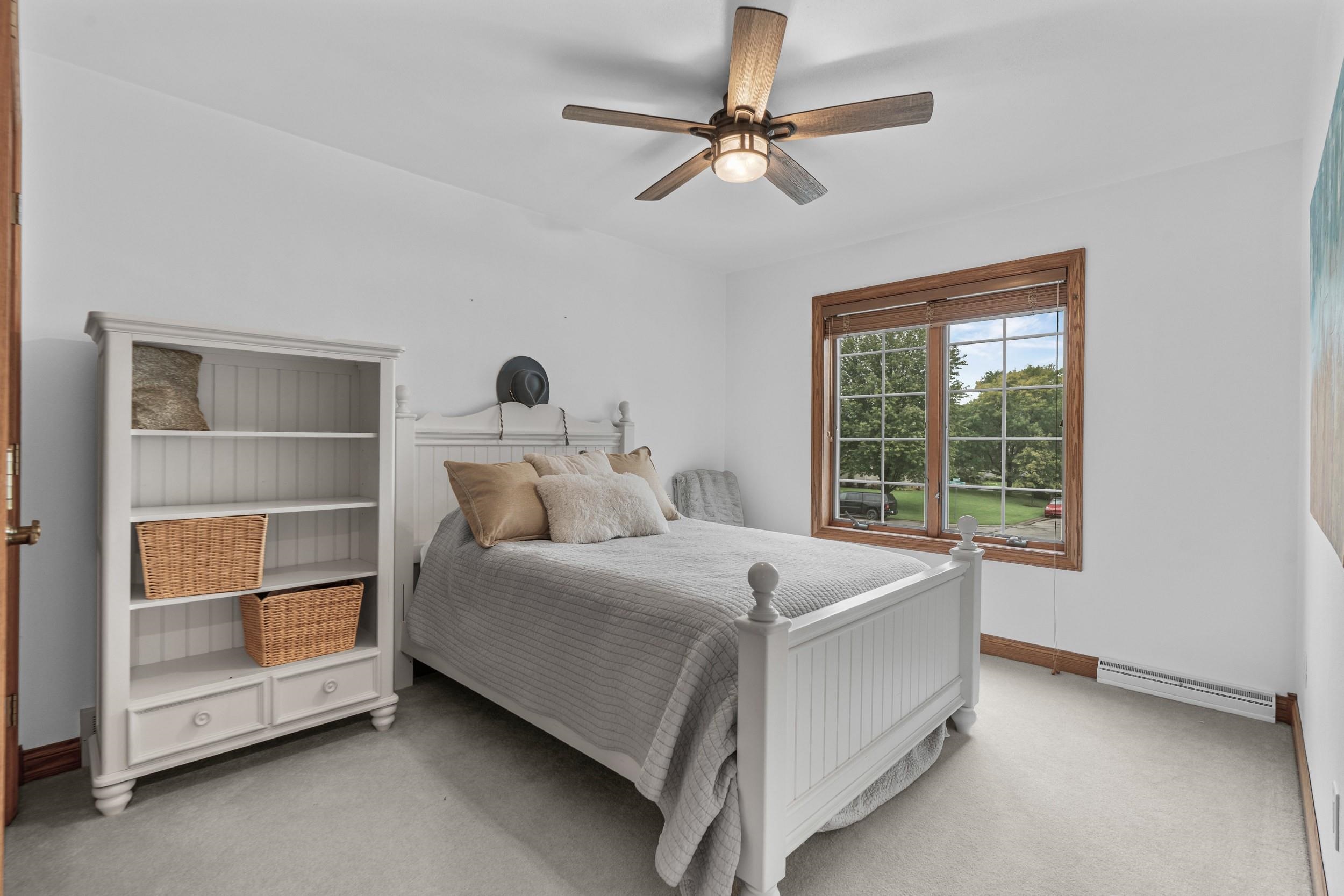 Furnished bedroom with a white paneled bed, wicker-basket shelving, and a wood-trimmed window overlooking trees.
