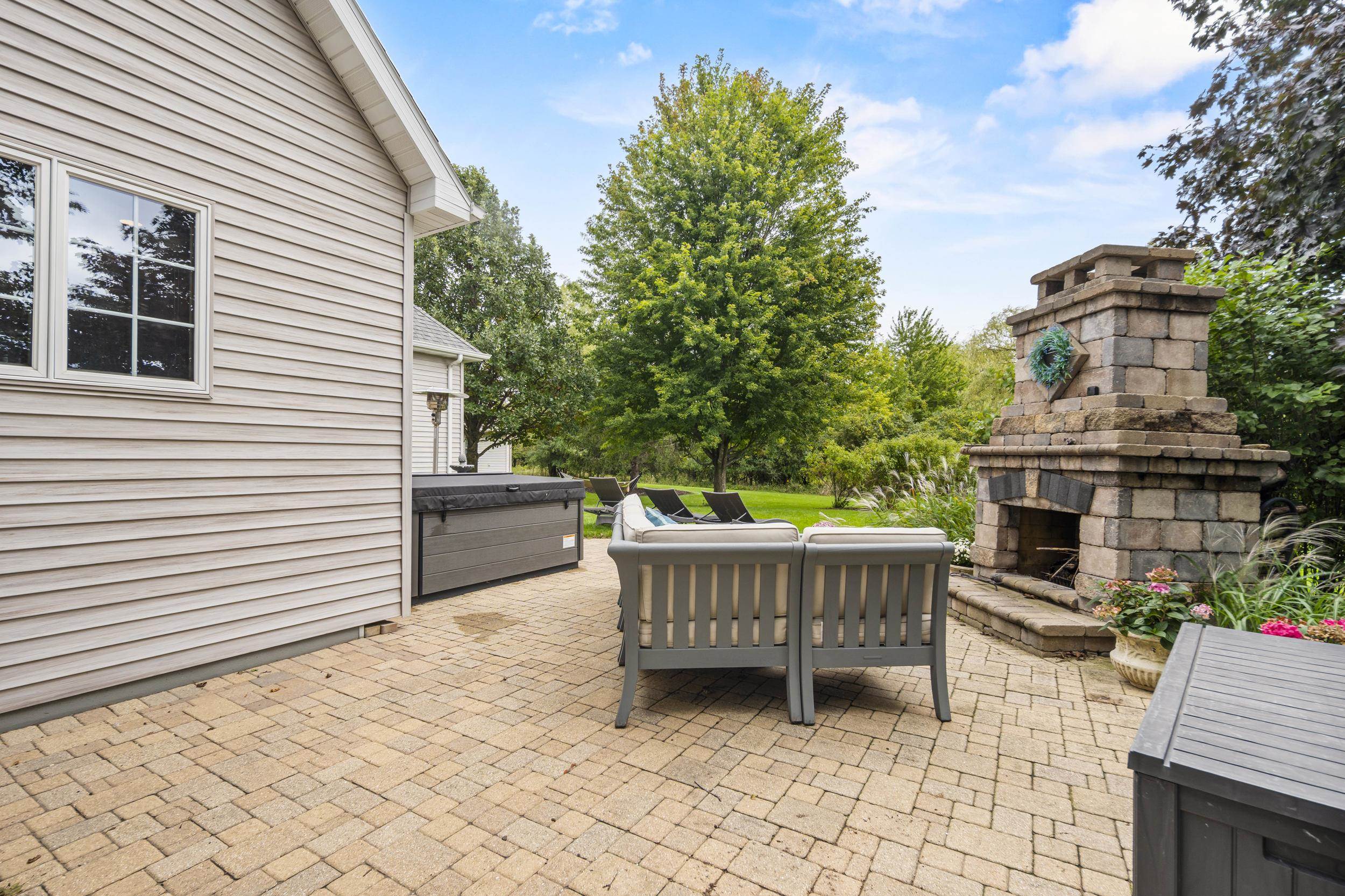 Backyard patio with a stone fireplace, hot tub, and outdoor lounge seating.
