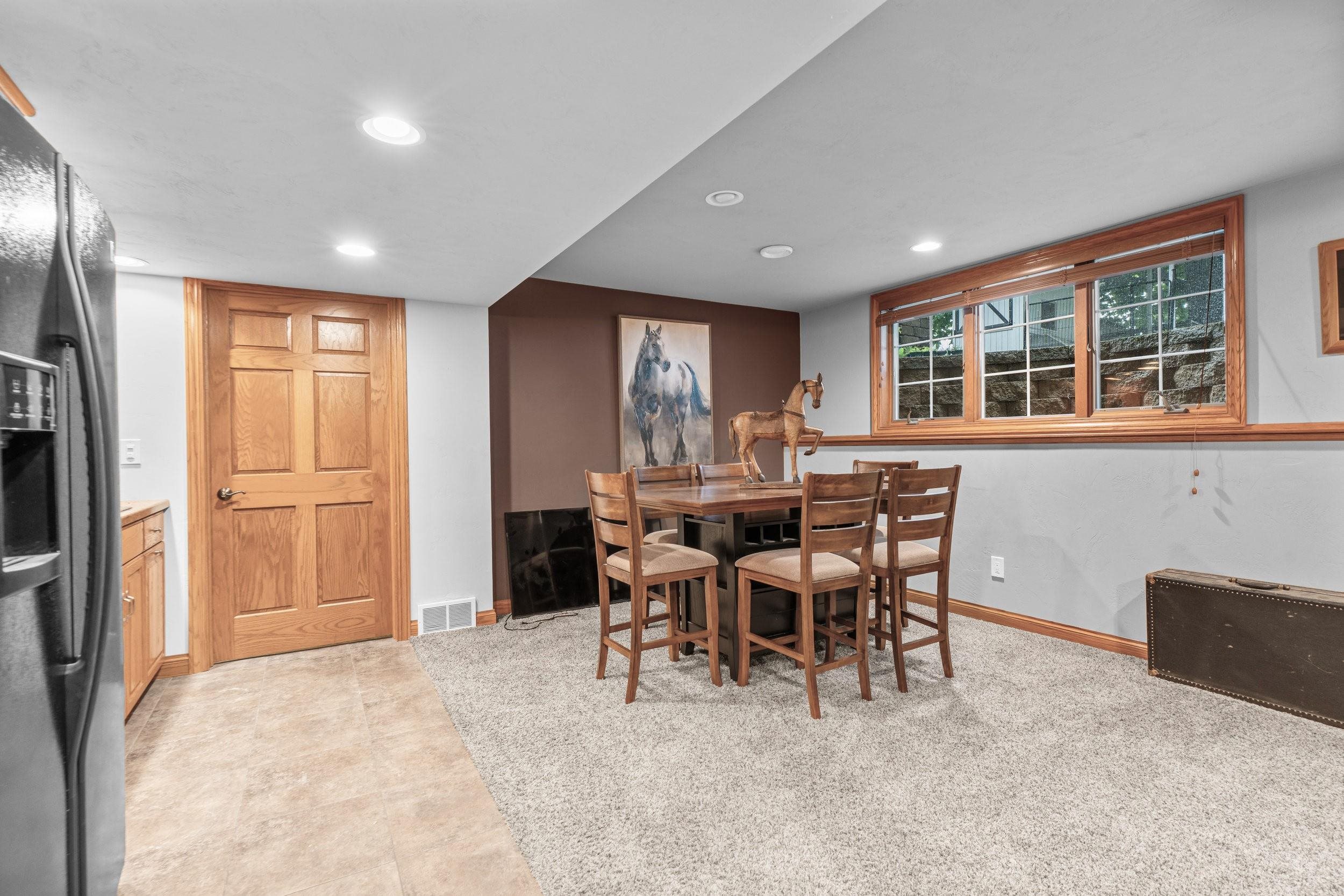 Furnished dining area with a wooden table beneath a large wood-trimmed window and horse artwork.