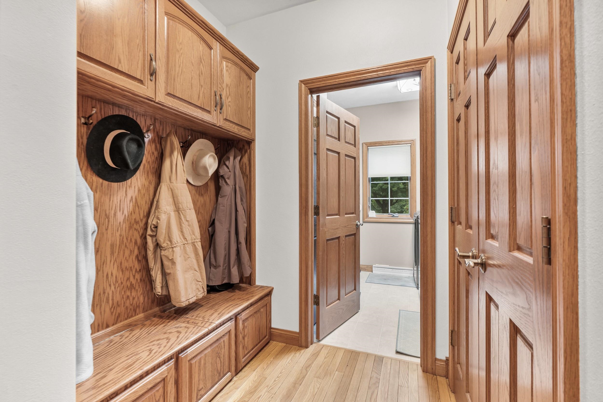 Mudroom with built-in oak cabinets, a bench, and hooks holding coats and hats.