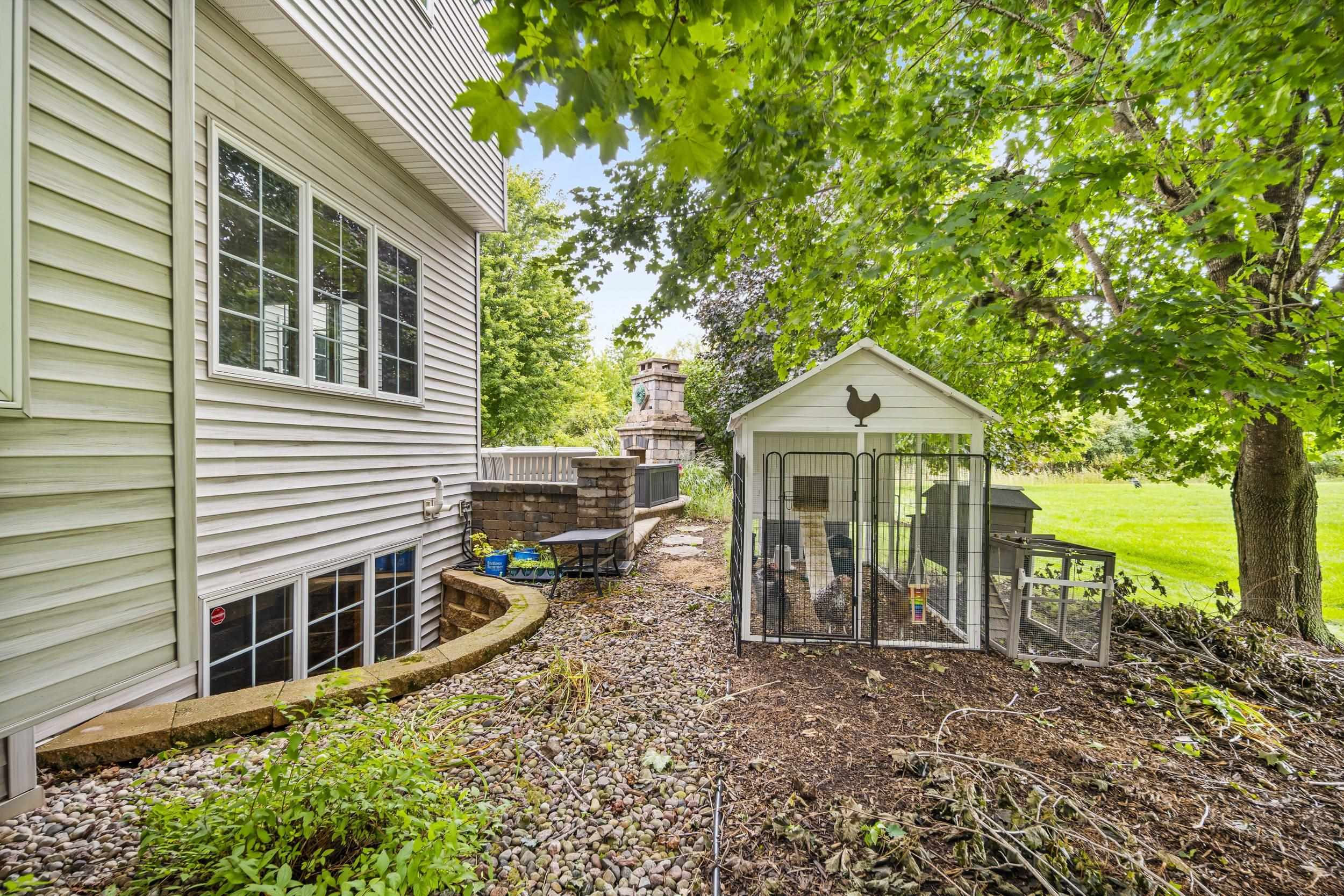 Home’s landscaped side yard with a stone fireplace, river-rock beds, and a white chicken coop.