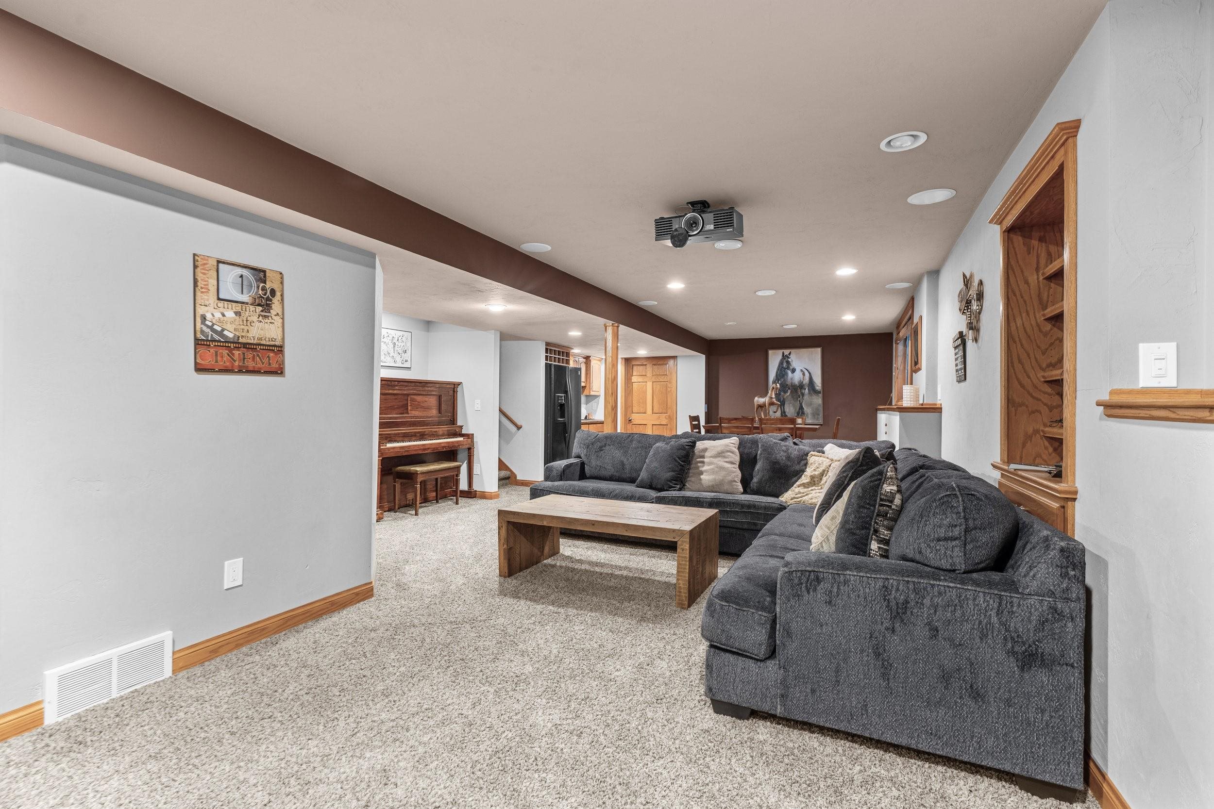 Basement media room with a charcoal sectional, ceiling-mounted projector, and piano.