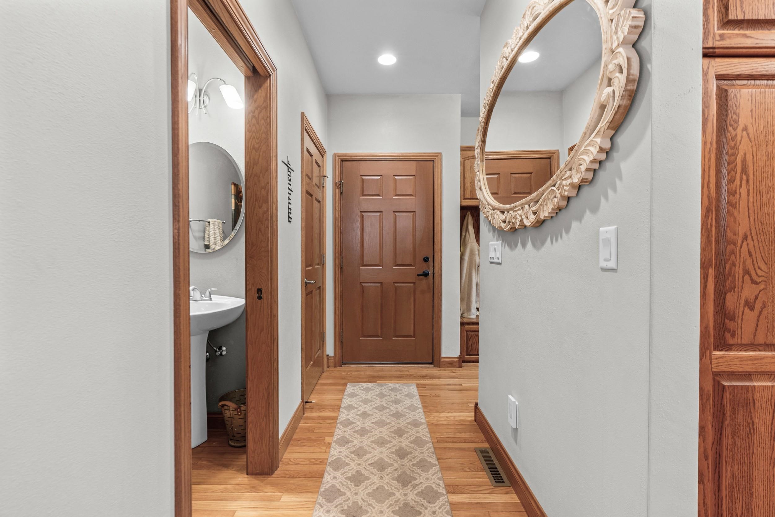 Hallway with hardwood floors, a patterned runner, wood doors, and an ornate oval mirror.