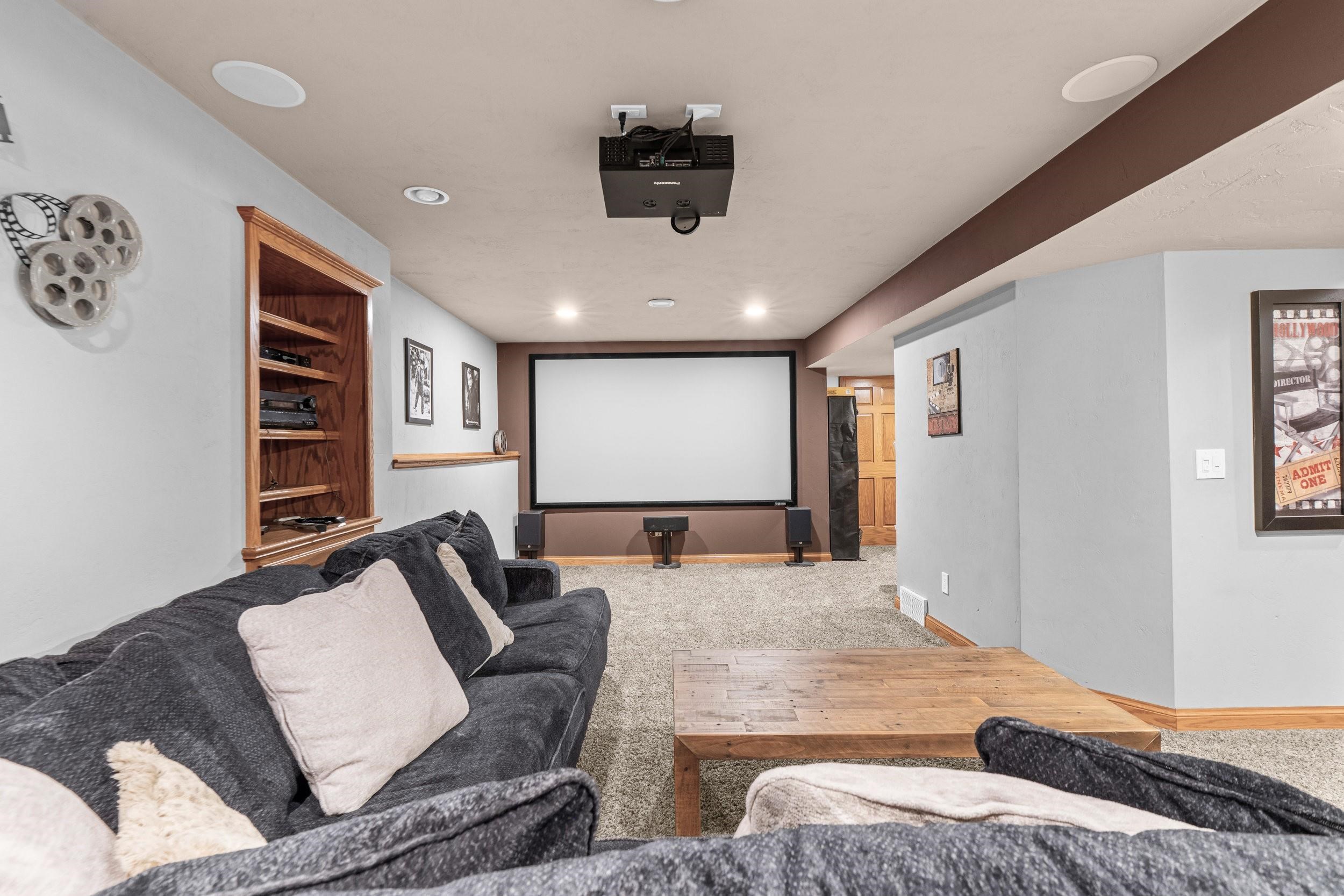 Home theater with a large projection screen, ceiling-mounted projector, surround speakers, and dark sectional sofas.