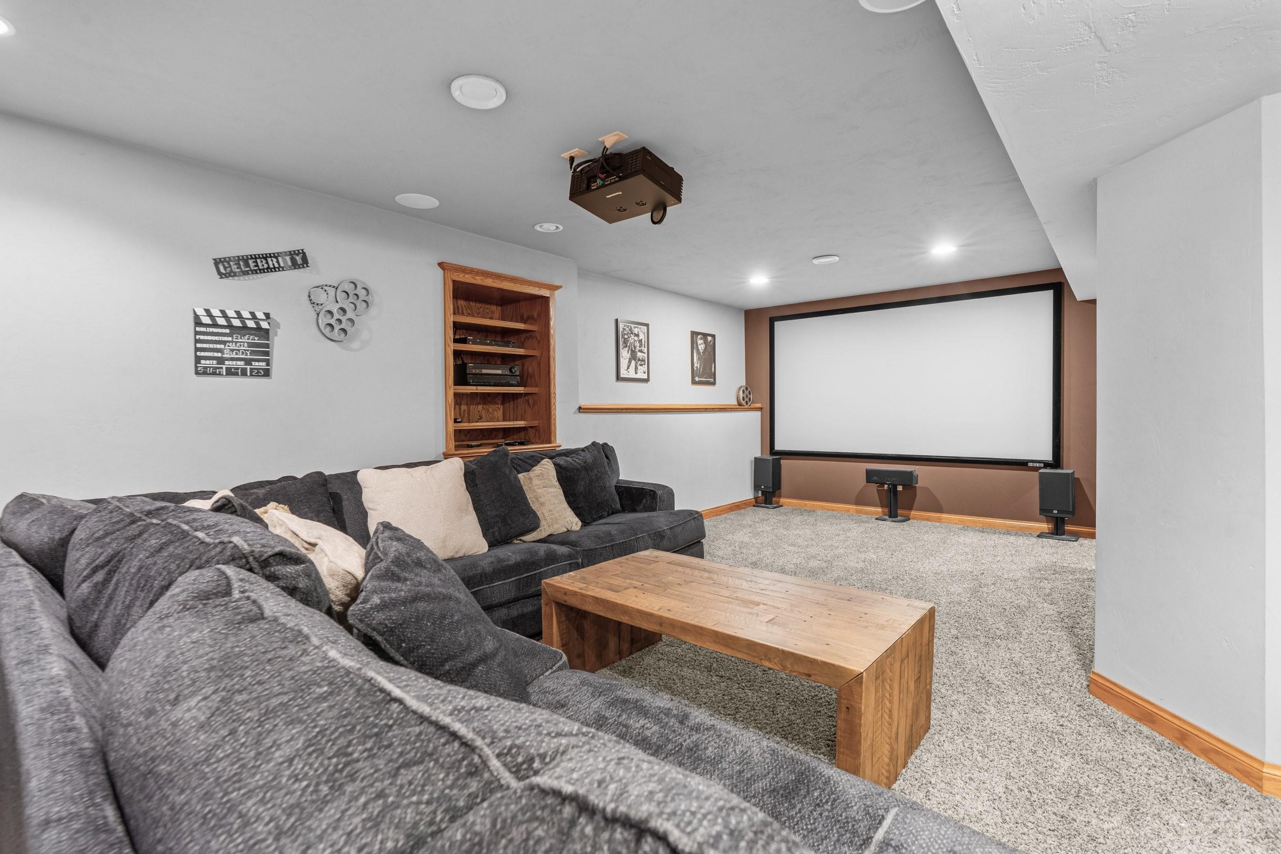 Furnished home theater with a large screen, ceiling projector, surround speakers, and sectional sofa.
