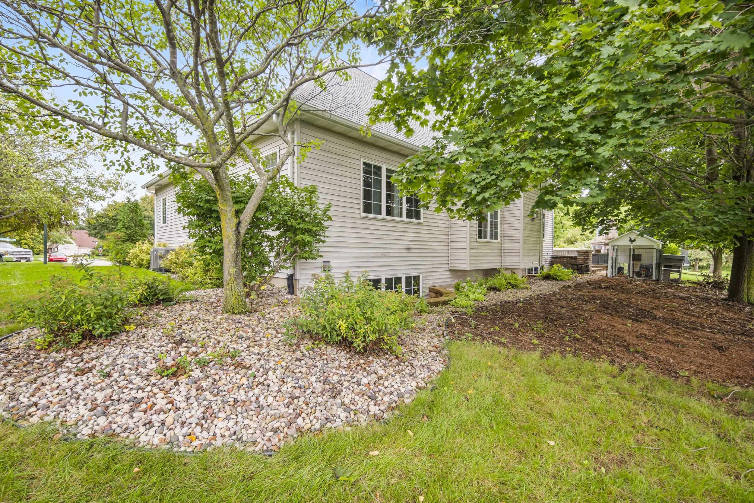 House exterior under mature trees, with a broad rock garden and a small outbuilding in the yard.