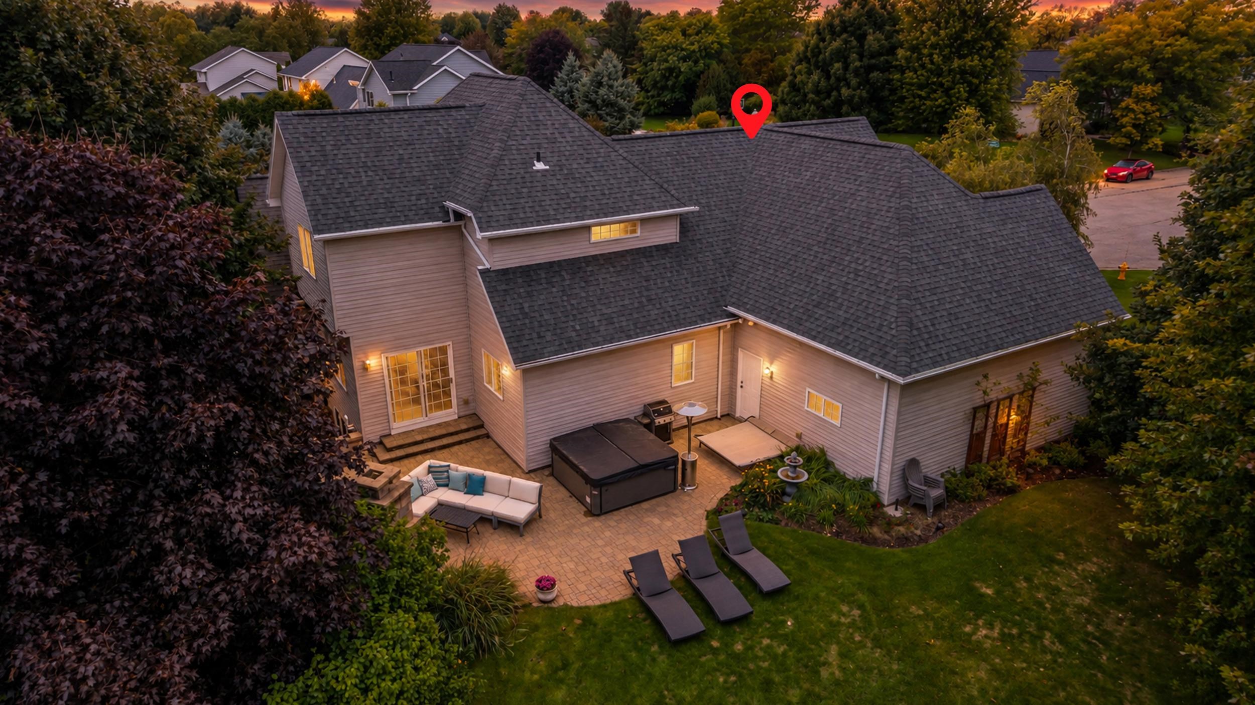 Aerial view of a house and landscaped backyard patio with a hot tub and outdoor seating at dusk.