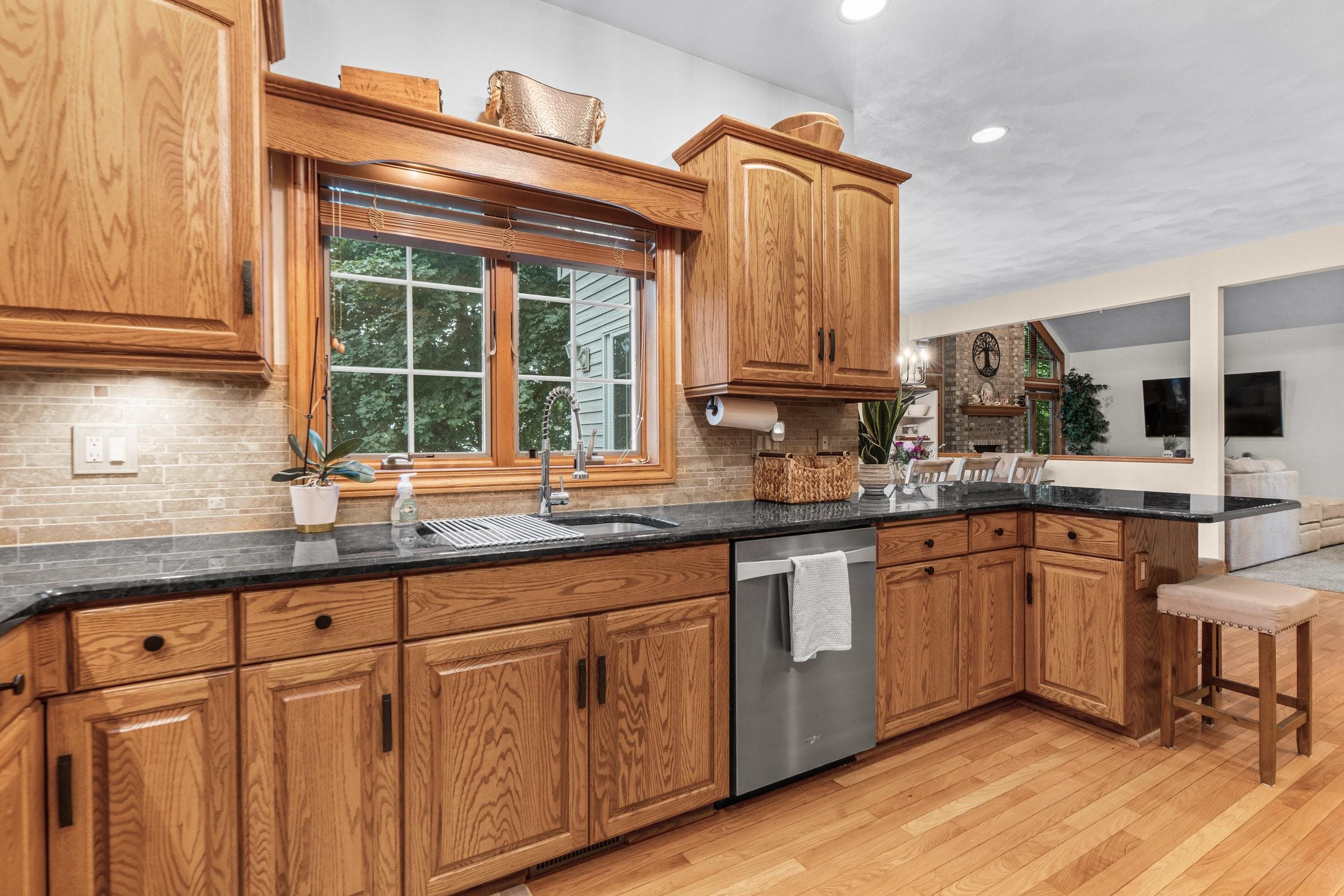 Kitchen with oak cabinets, black countertops, a window above the sink, and a breakfast bar.