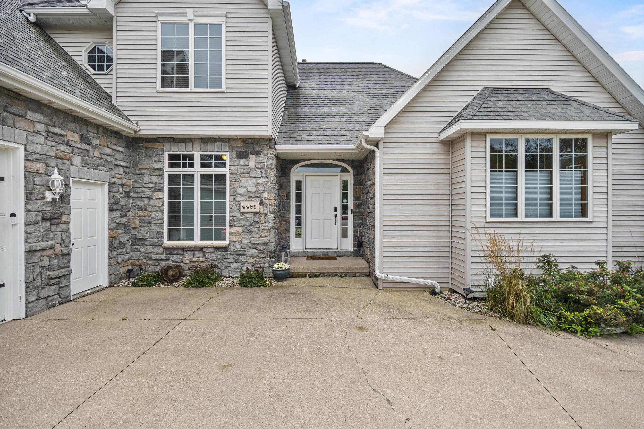 Home exterior with stone entry facade, light siding, and a wide concrete driveway.
