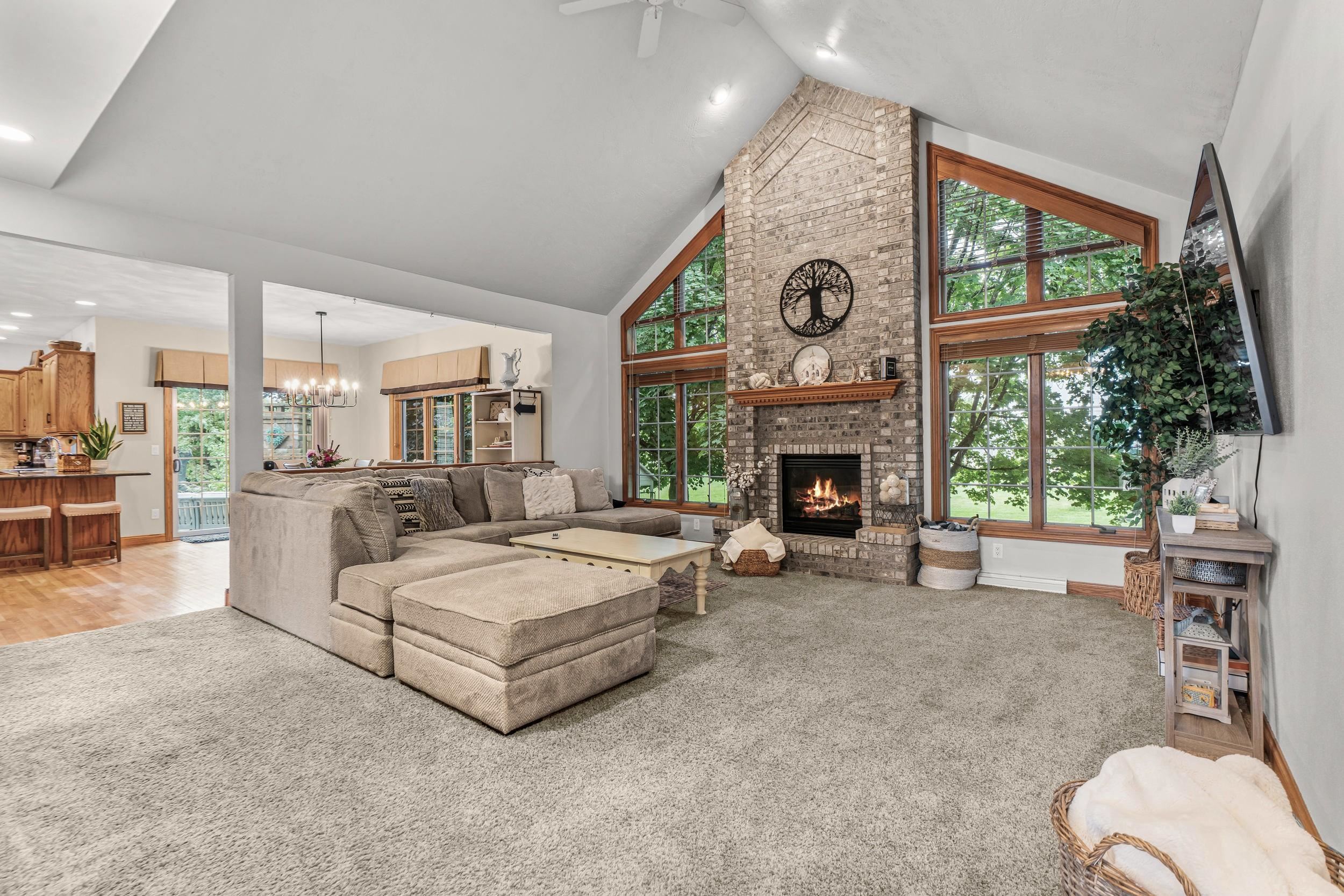 Vaulted living room with a tall brick fireplace, large windows, and a gray sectional sofa.