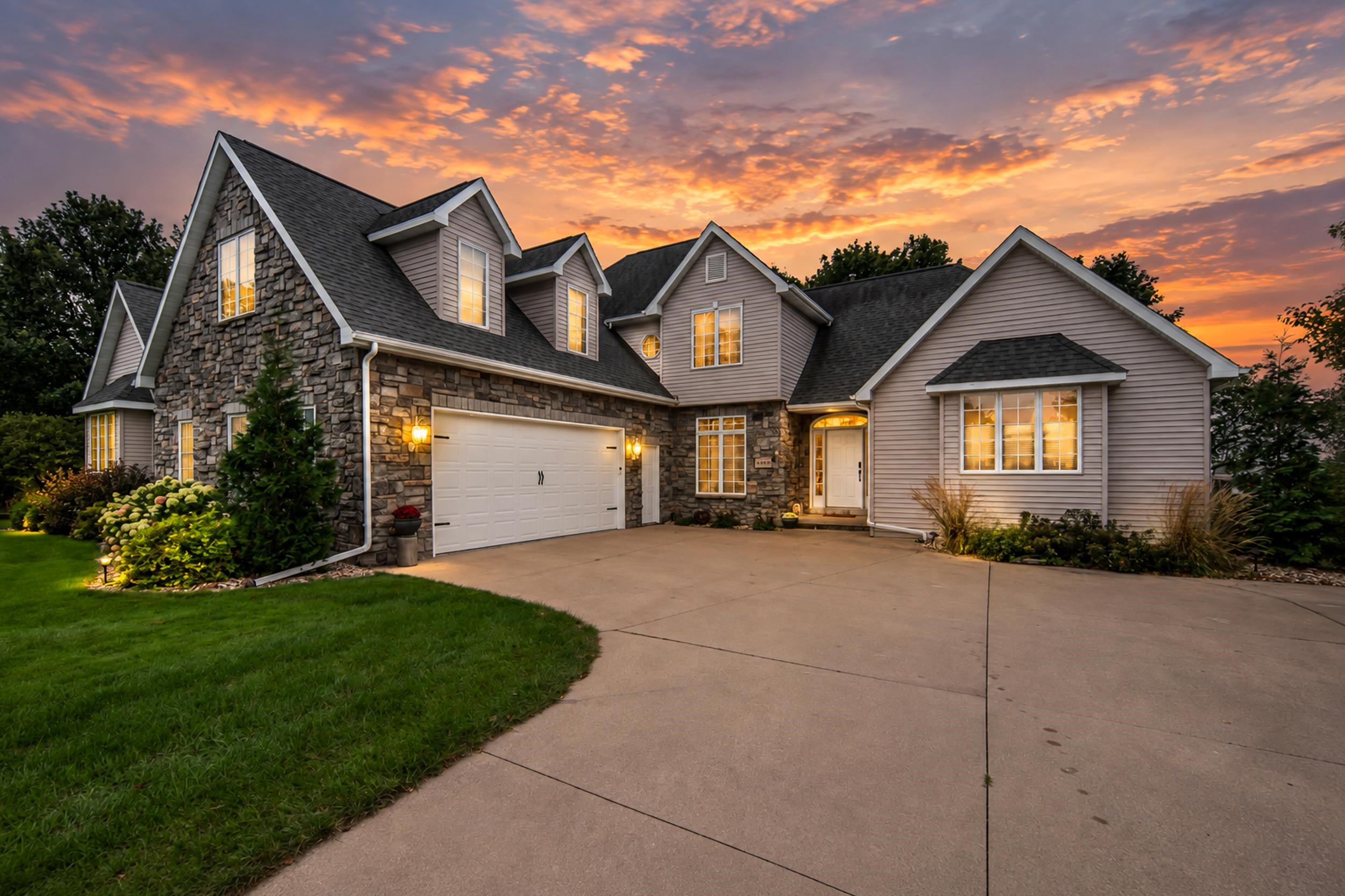 Two-story stone-and-siding home with a double garage and illuminated windows at dusk.