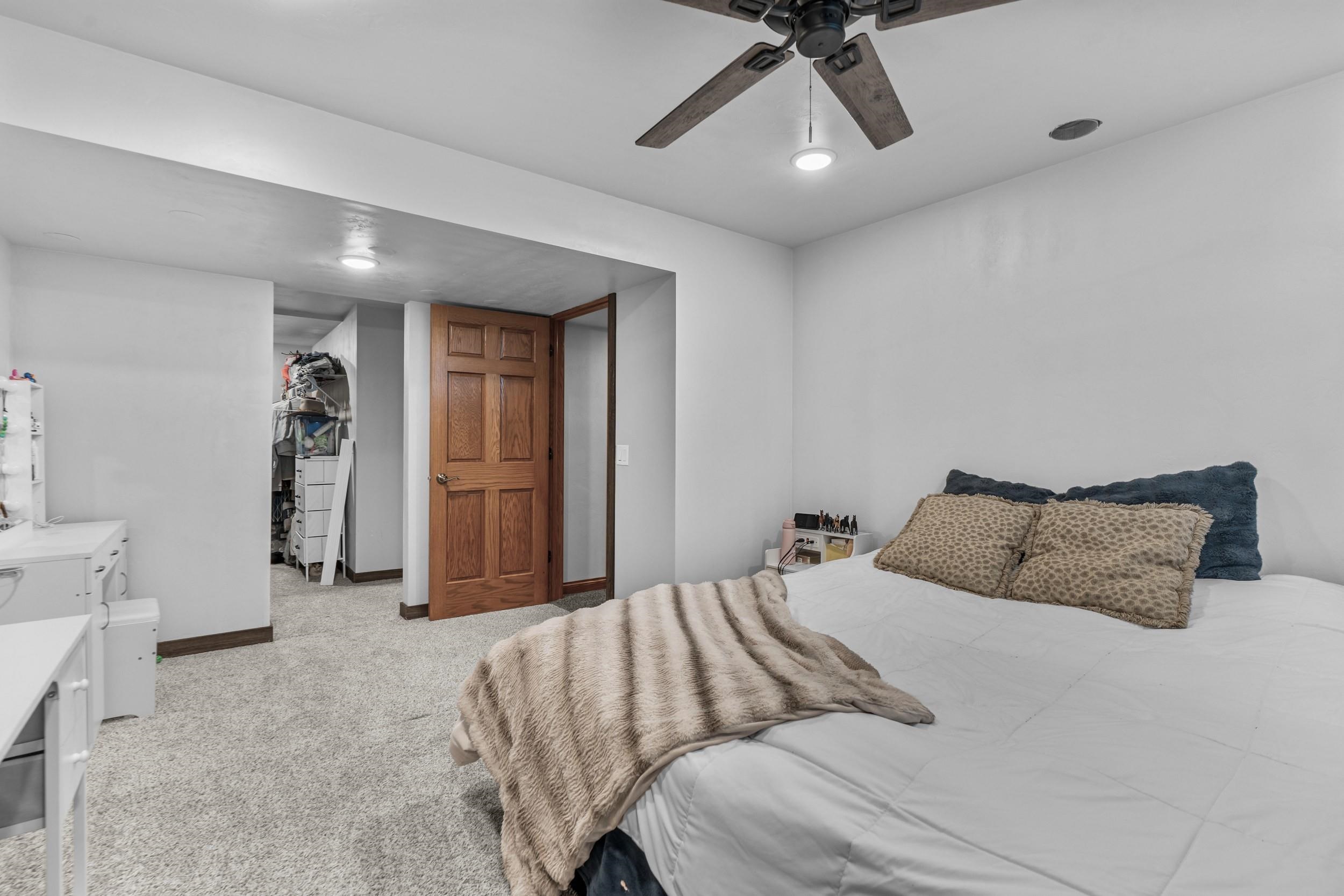 Furnished bedroom with a large bed, beige throw, ceiling fan, and open walk-in closet.
