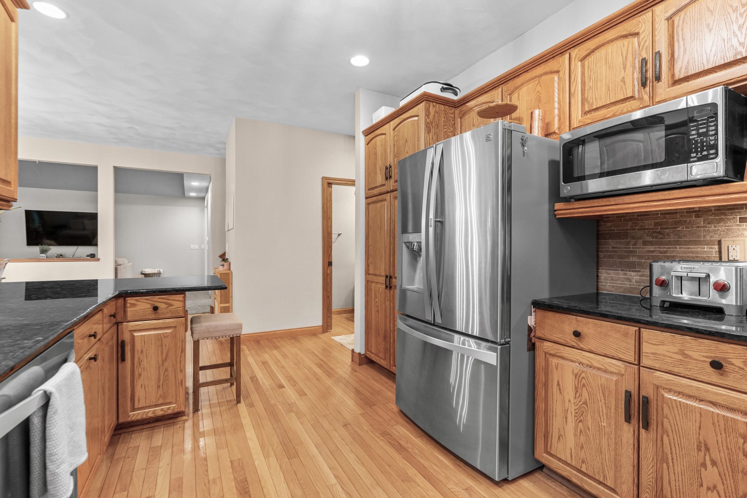 Kitchen with oak cabinets, hardwood floors, black countertops, and stainless steel appliances.