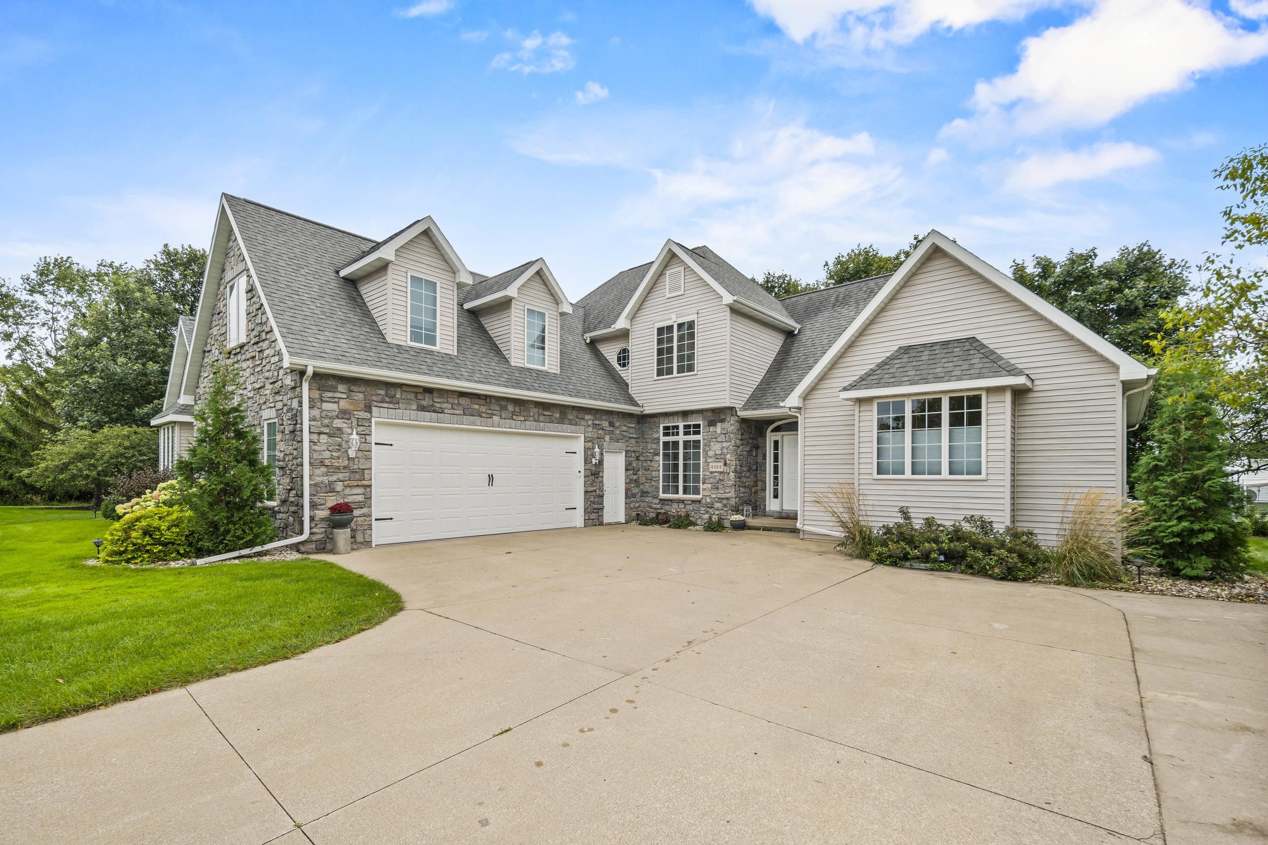 Two-story stone-and-siding home with multiple gables, a two-car garage, and a broad concrete driveway.