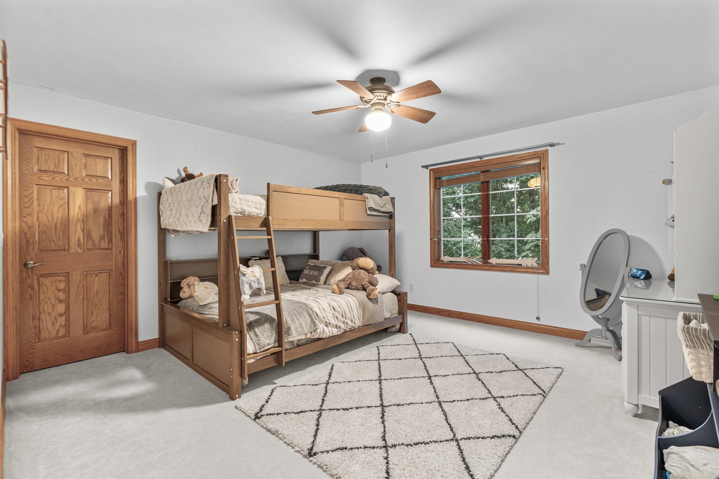 Bedroom with a wooden bunk bed, plush toys, a leafy window view, and a geometric rug.