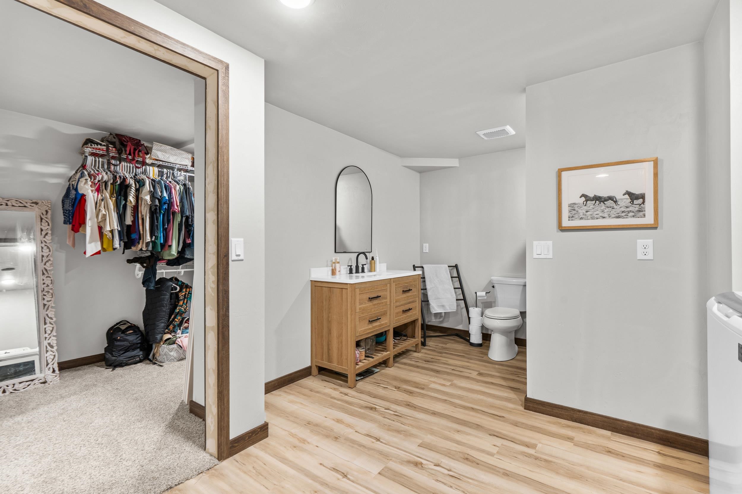 Bathroom with a wood vanity and walk-in closet filled with hanging clothes.