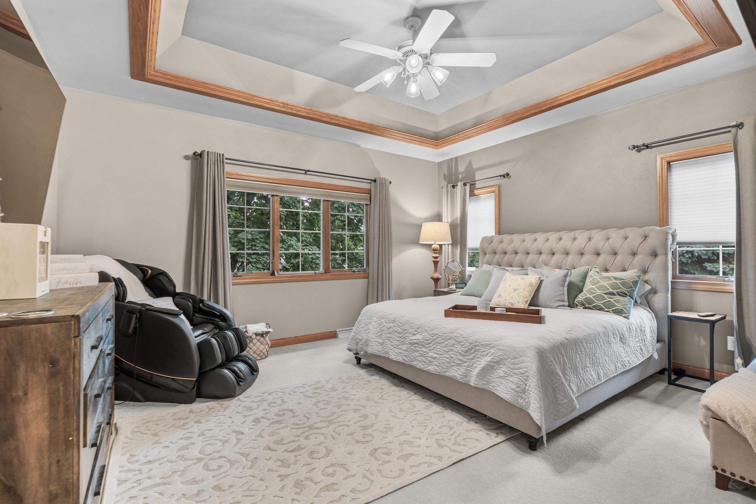 Bedroom with a tufted bed, massage chair, and wood-trimmed tray ceiling.