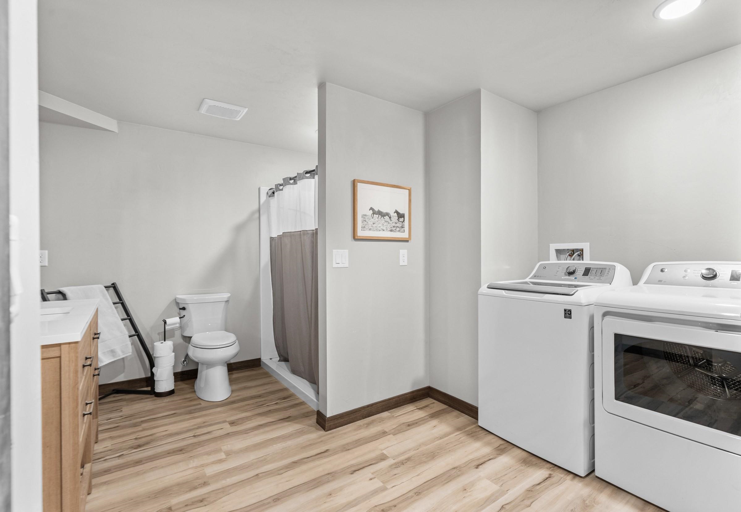 Combined bathroom and laundry room with a shower, wood vanity, toilet, washer, and dryer.