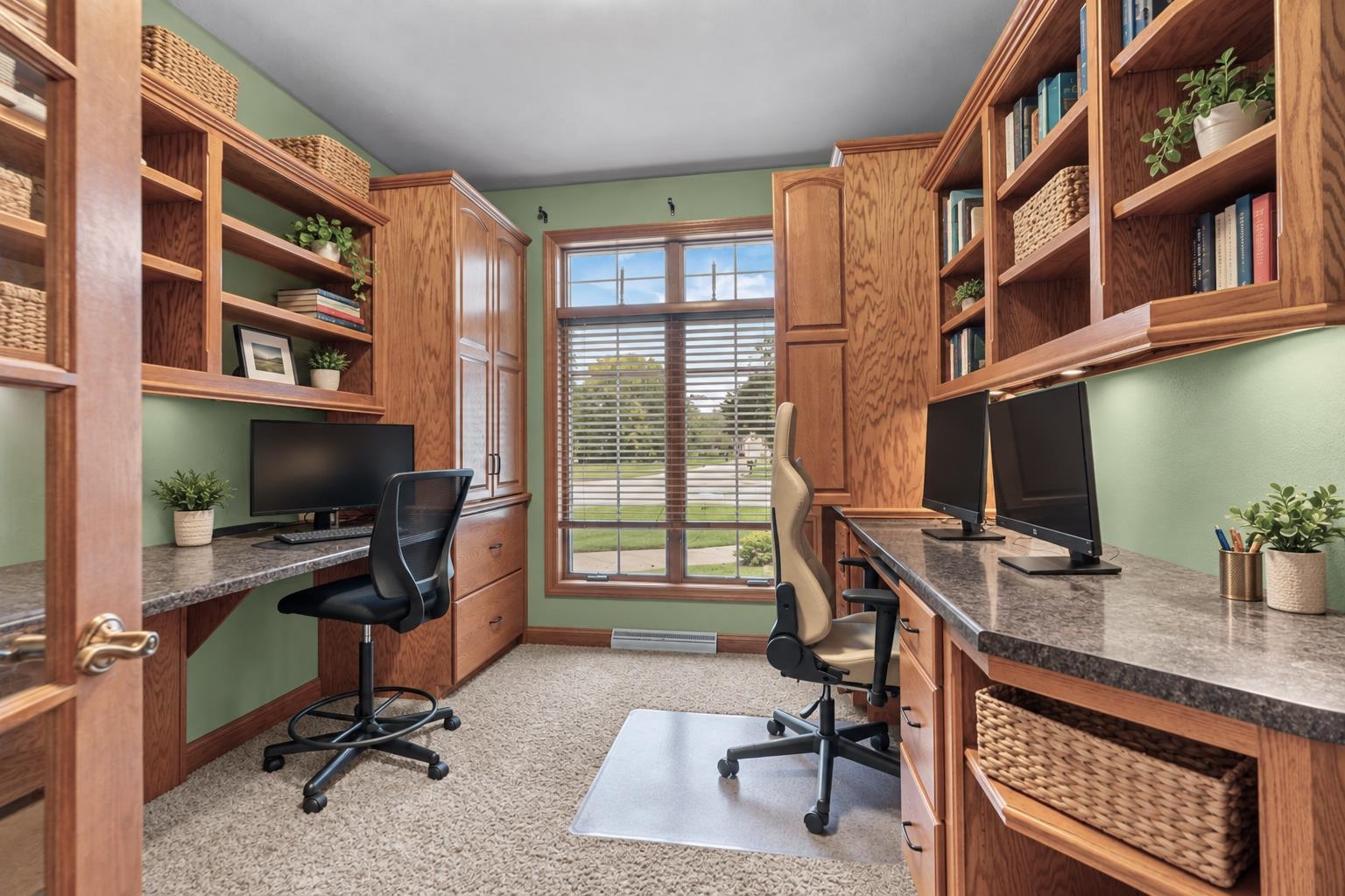 Home office with two built-in desks, oak bookshelves, and a large window with blinds.