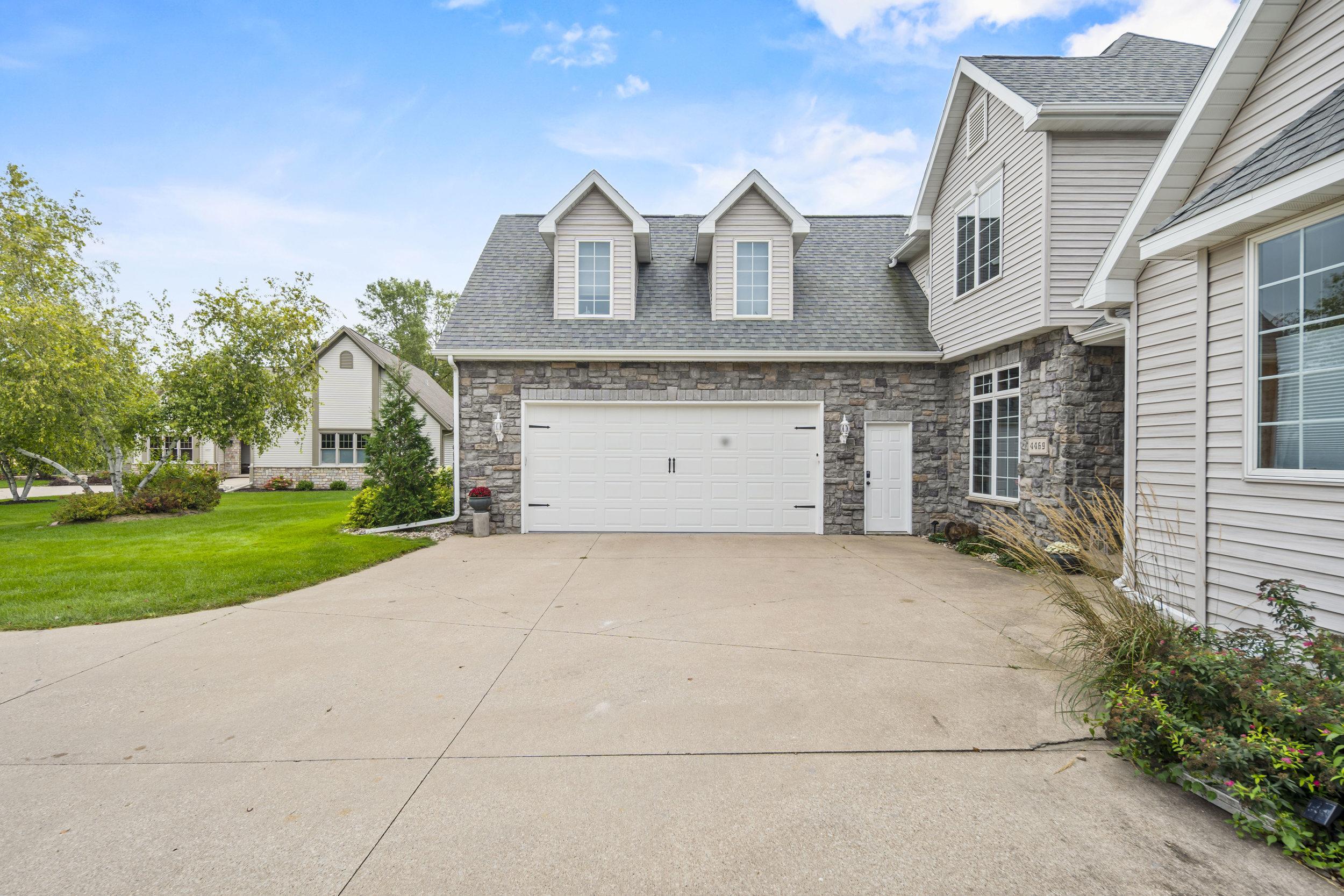Home exterior with stone facade, white garage door, and broad concrete driveway.