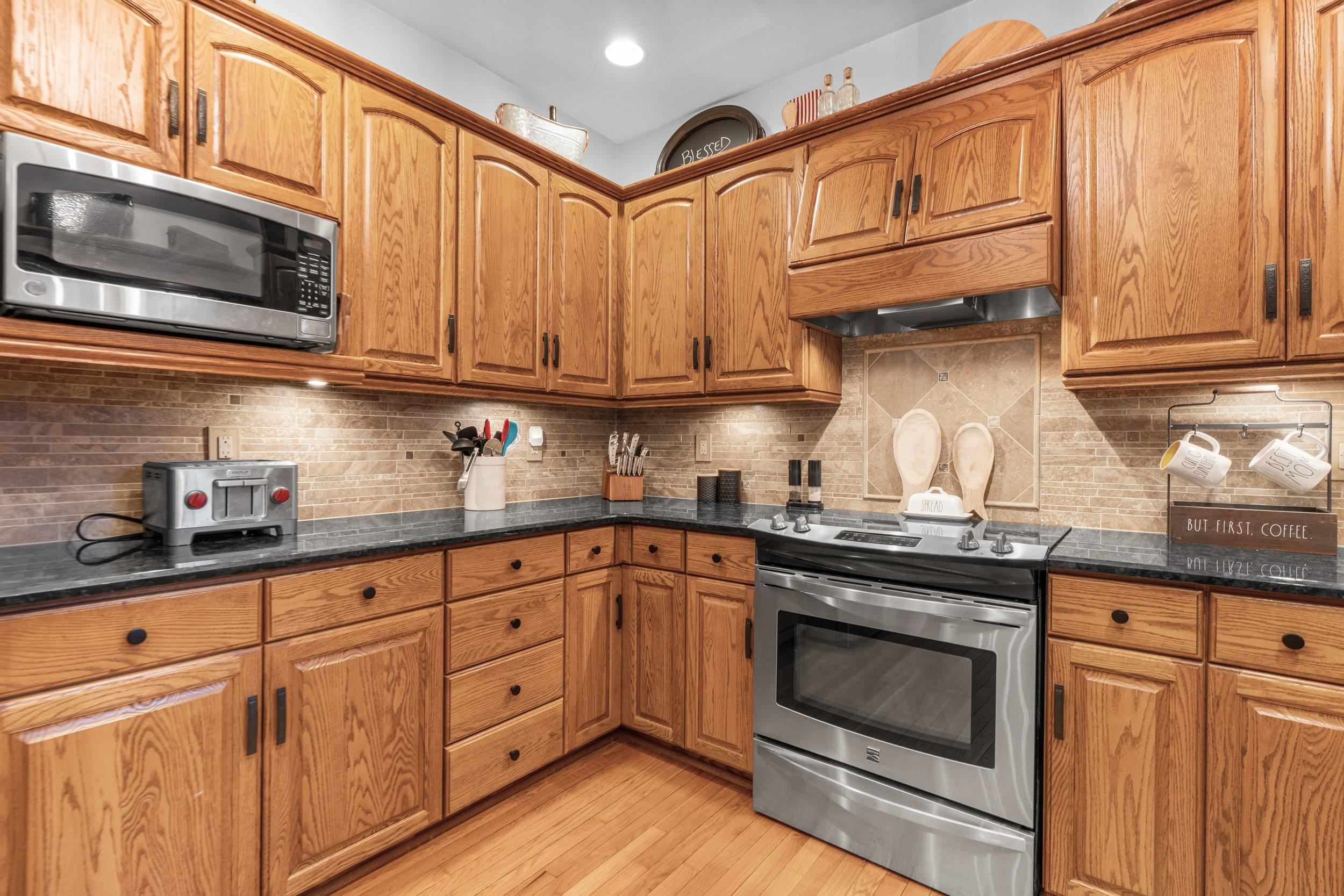 Kitchen with honey-toned oak cabinets, dark countertops, and stainless steel appliances.