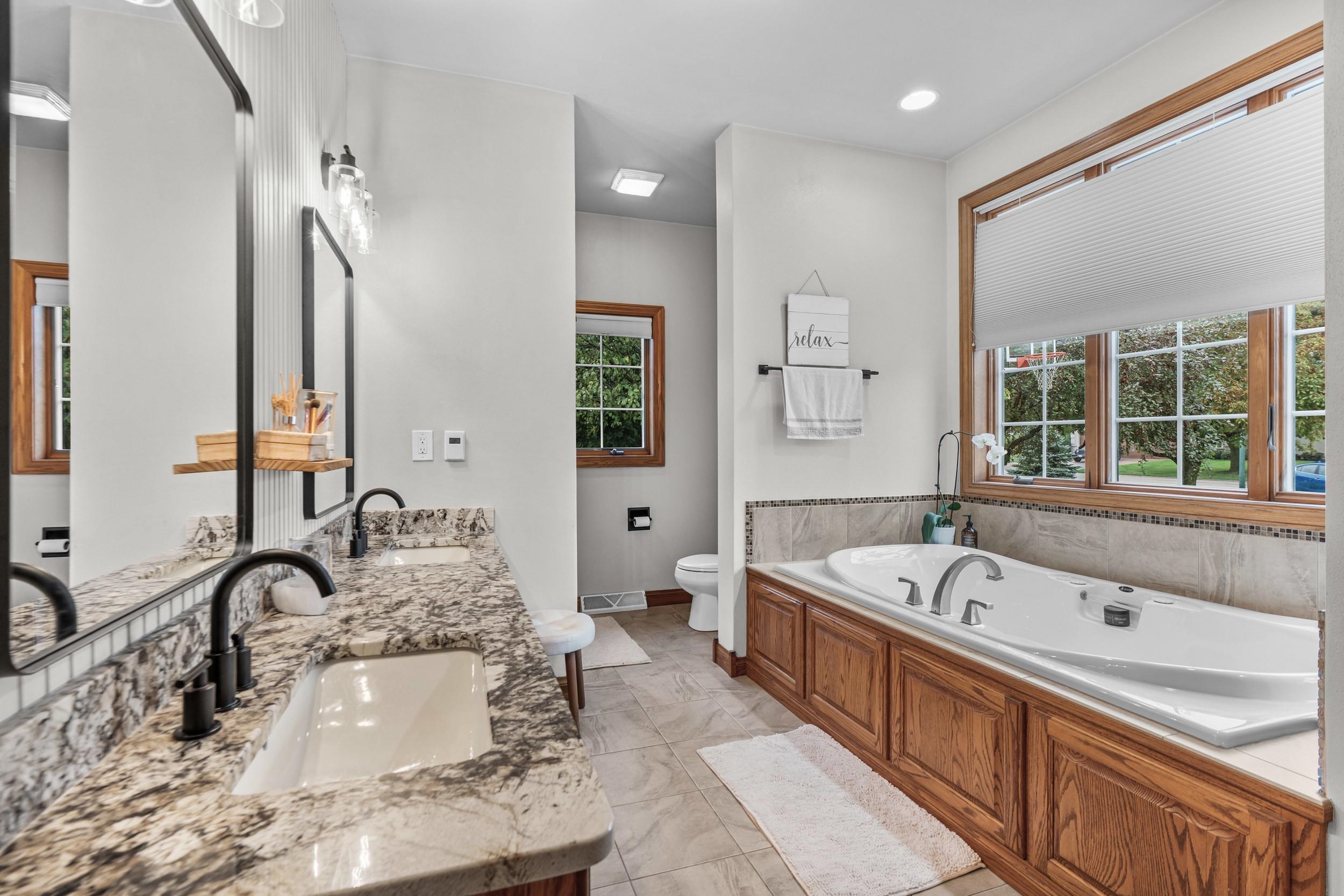 Primary bathroom with a wood-paneled jetted tub beneath large windows and a double stone-counter vanity.