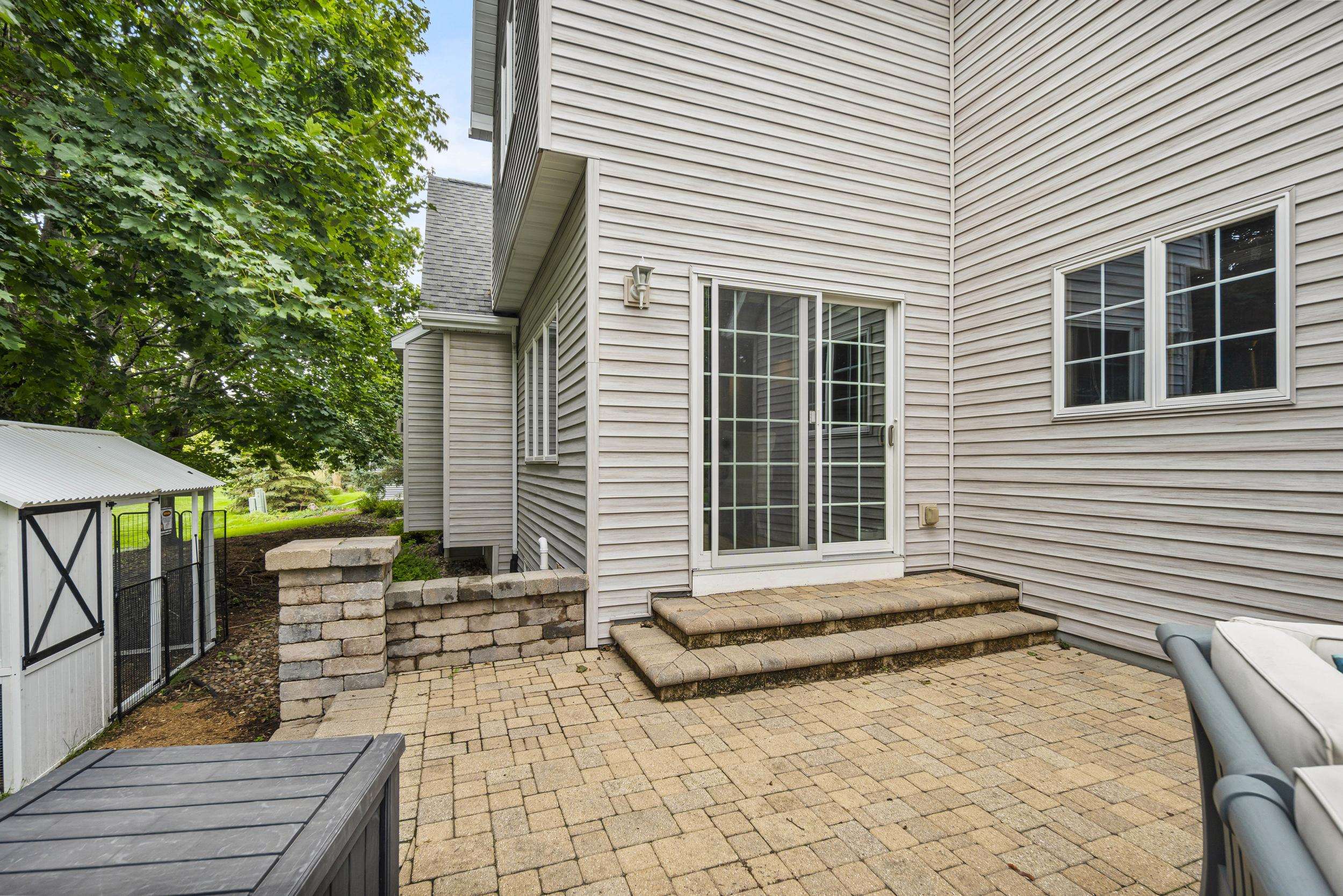 House patio with sliding glass doors, brick steps, and a low retaining wall beside a small shed.