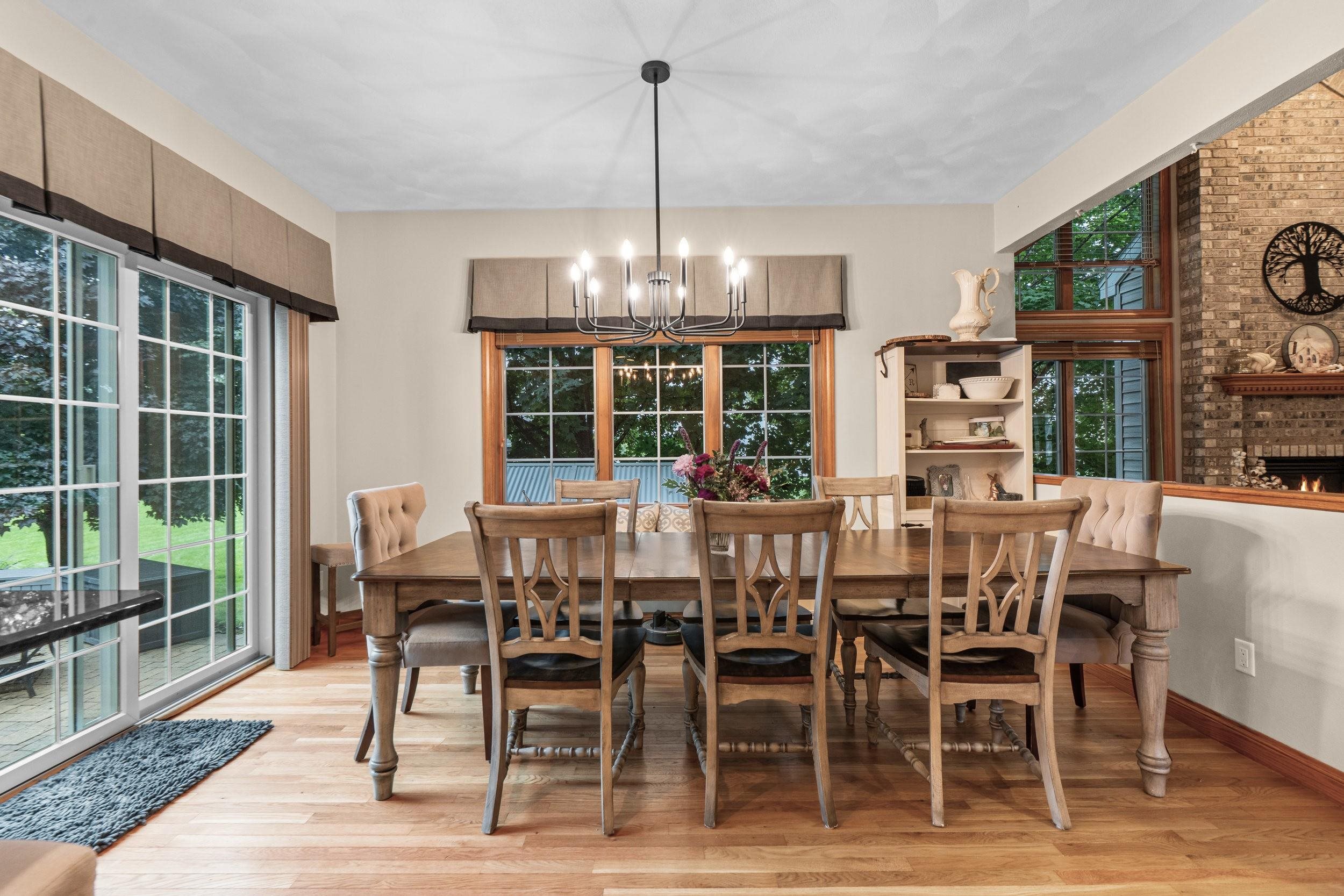 Dining room with a large wooden table, chandelier, tall windows, and brick fireplace