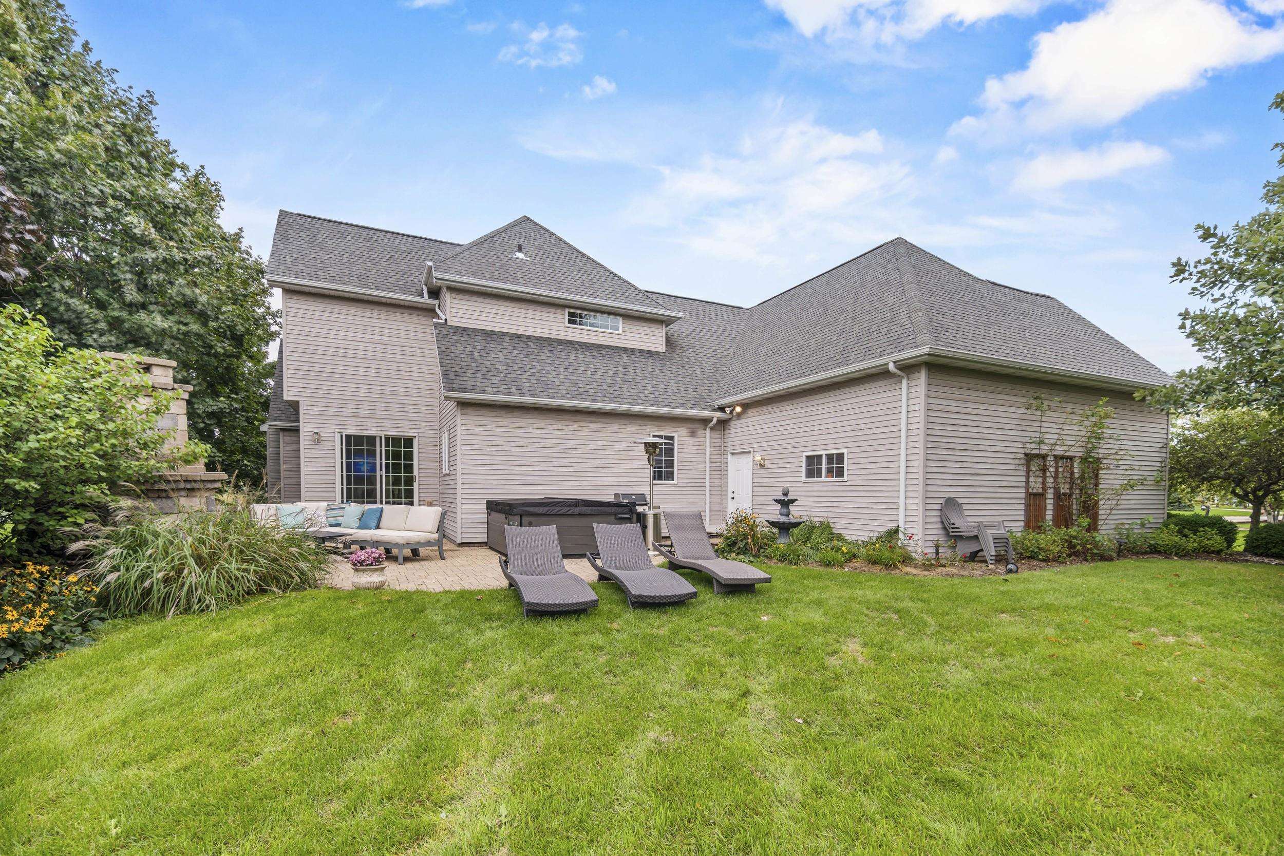 Rear of a gray-sided house with a patio, hot tub, outdoor seating, and broad green lawn.